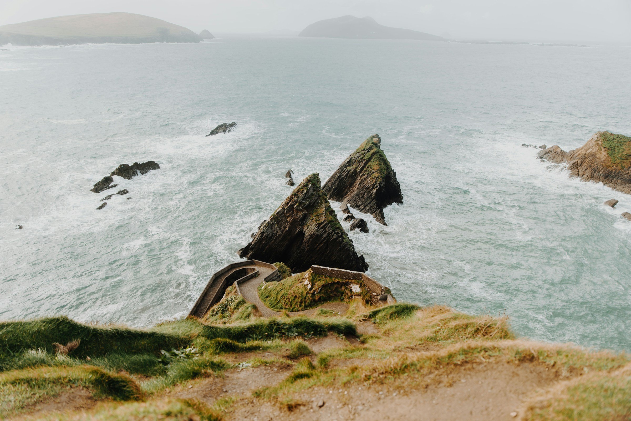Aerial view of dramatic cliffs at Dunquin Pier on the Dingle Peninsula in Ireland, with rugged rock formations surrounded by the Atlantic Ocean's waves.