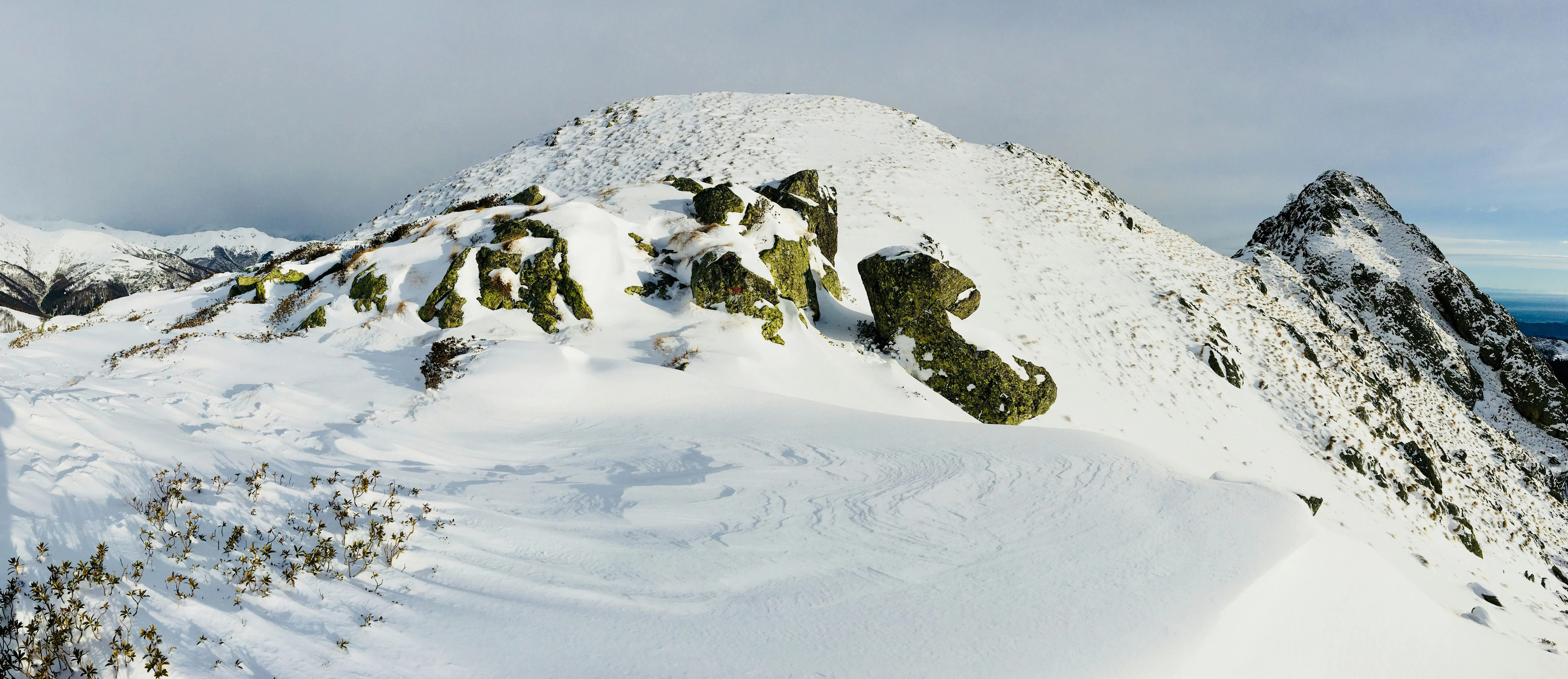 Snow-capped mountain peak with mossy cliffs under a cloudy sky in Alagna, Italy.