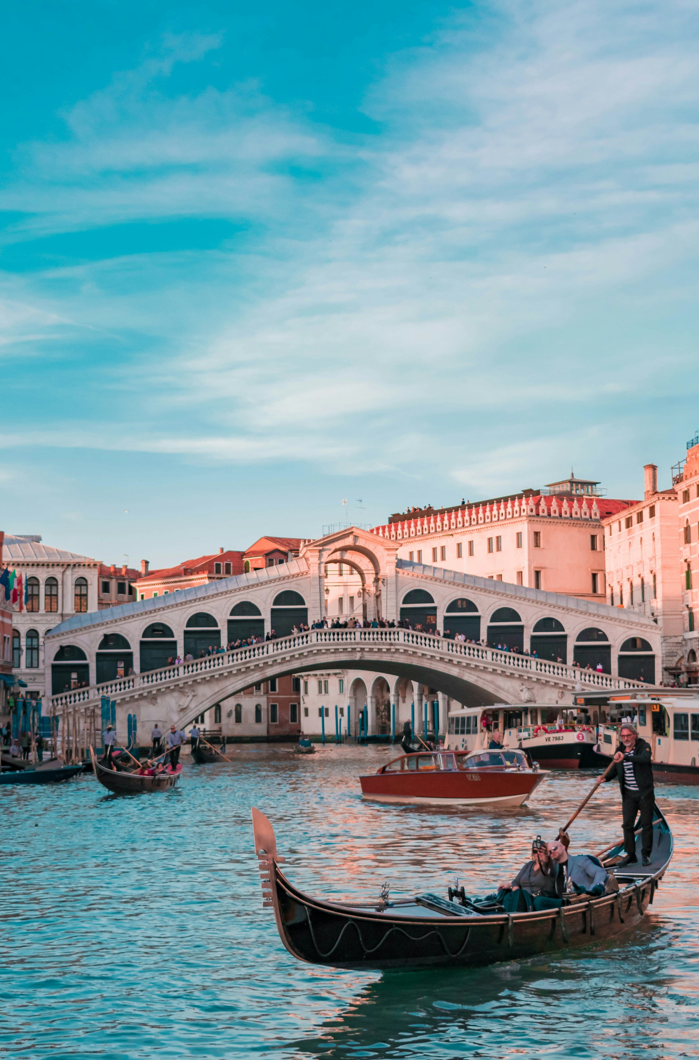 Gondola ride on the Grand Canal in Venice with the historic Rialto Bridge in the background under a clear blue sky.