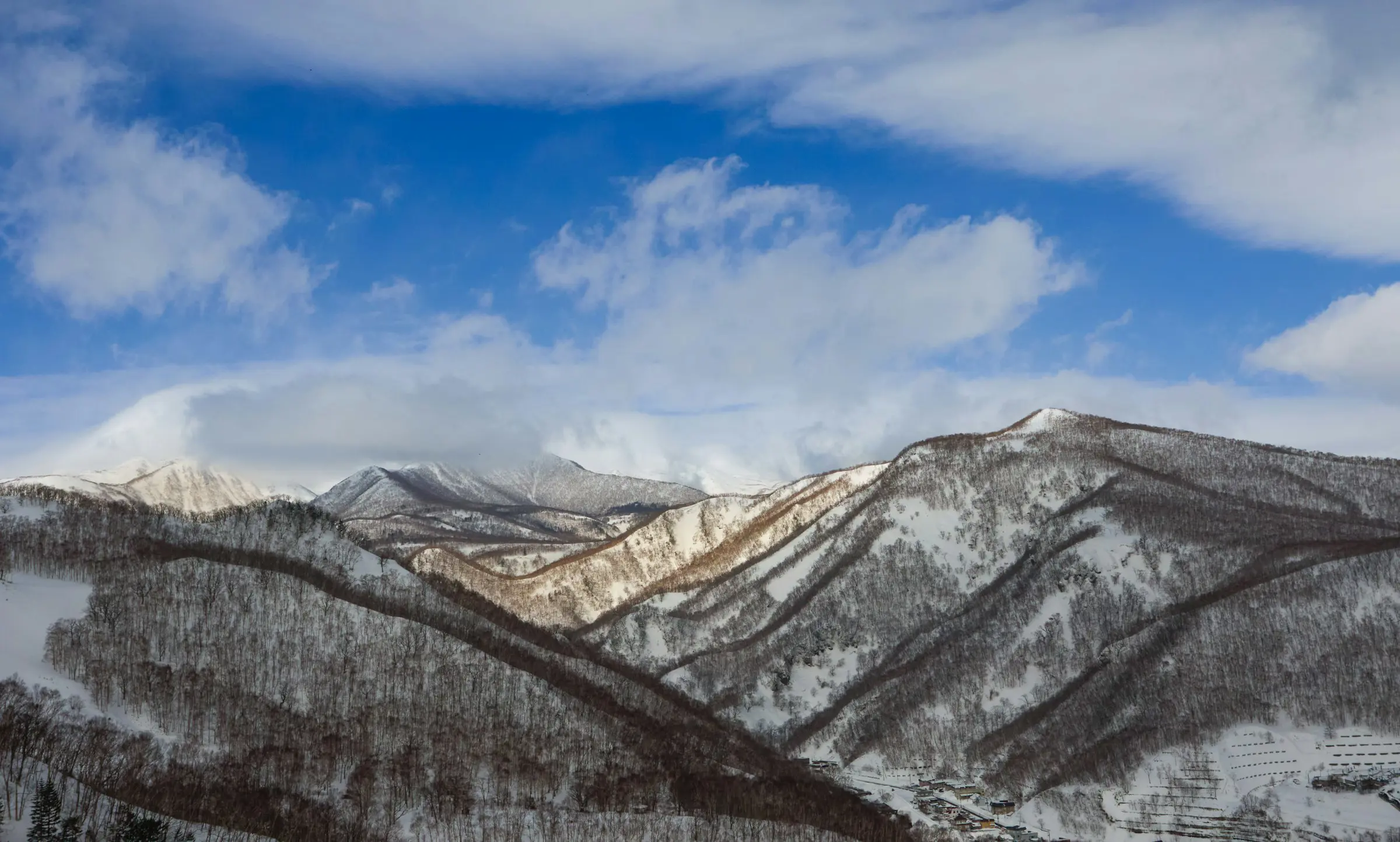 Snødekte fjell under en klar blå himmel med skyer i Hokkaido, Japan.