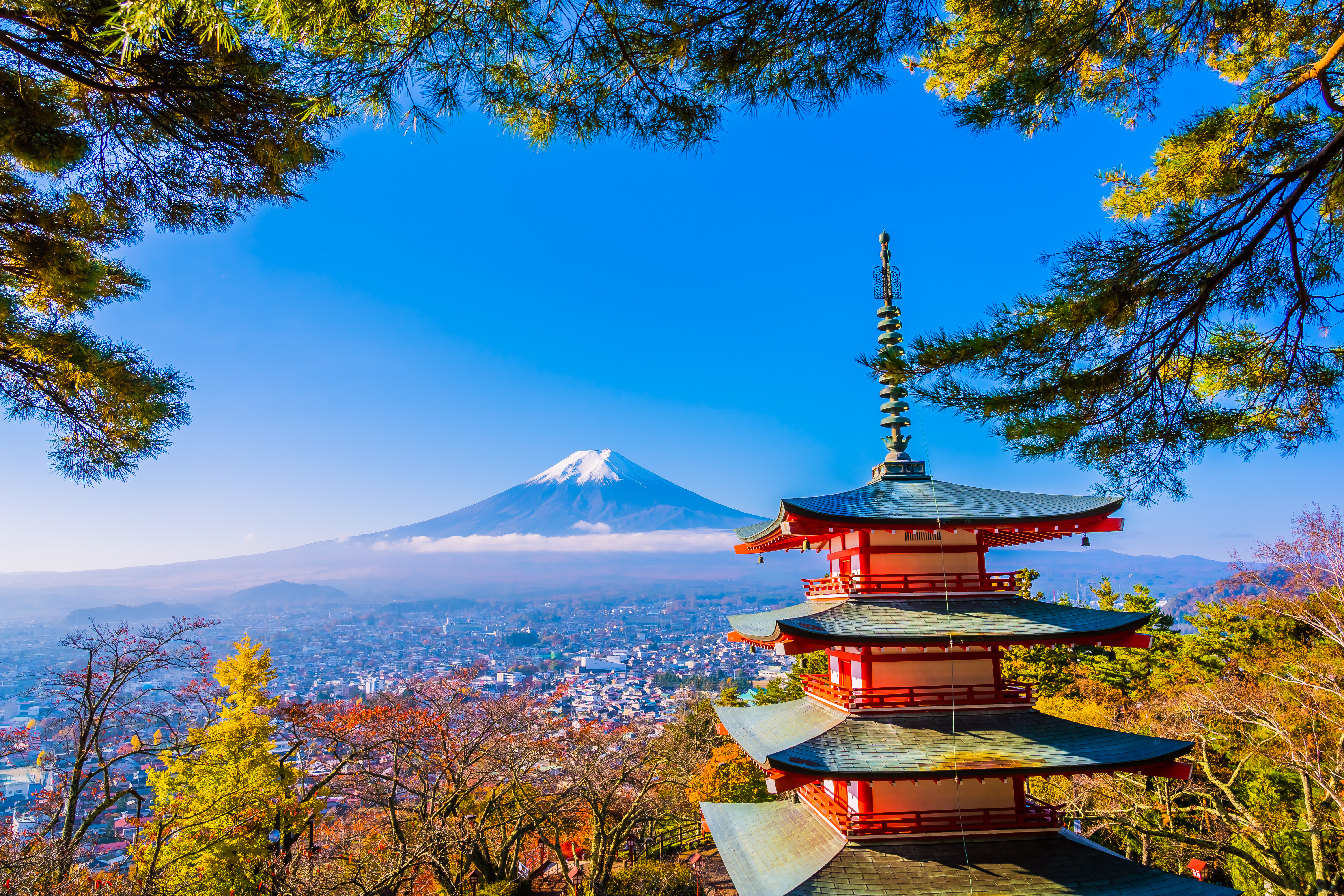 Travel to Japan - Chureto Pagoda and Mt Fuji in the background with clear blue skies in Japan, surrounded by green trees and overlooking a city.