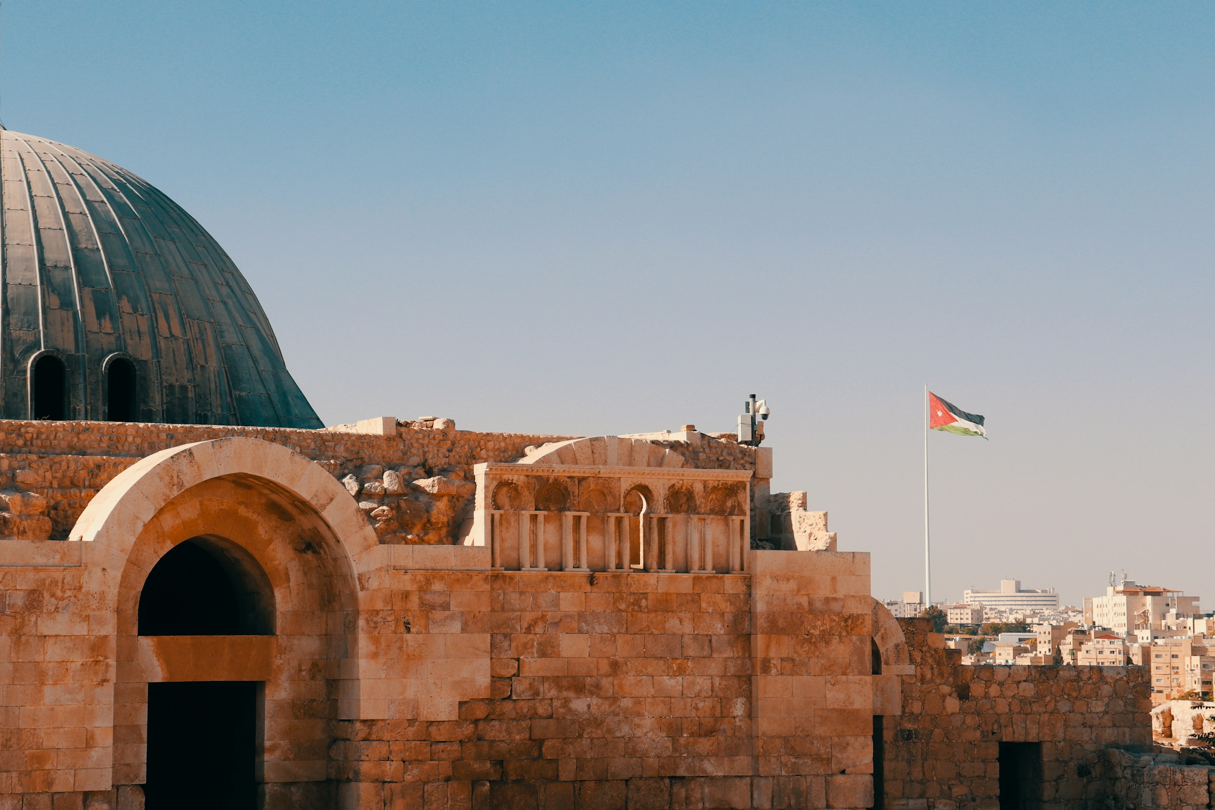 Historic Citadel of Amman with Jordanian flag, showcasing ancient architecture under a clear blue sky.