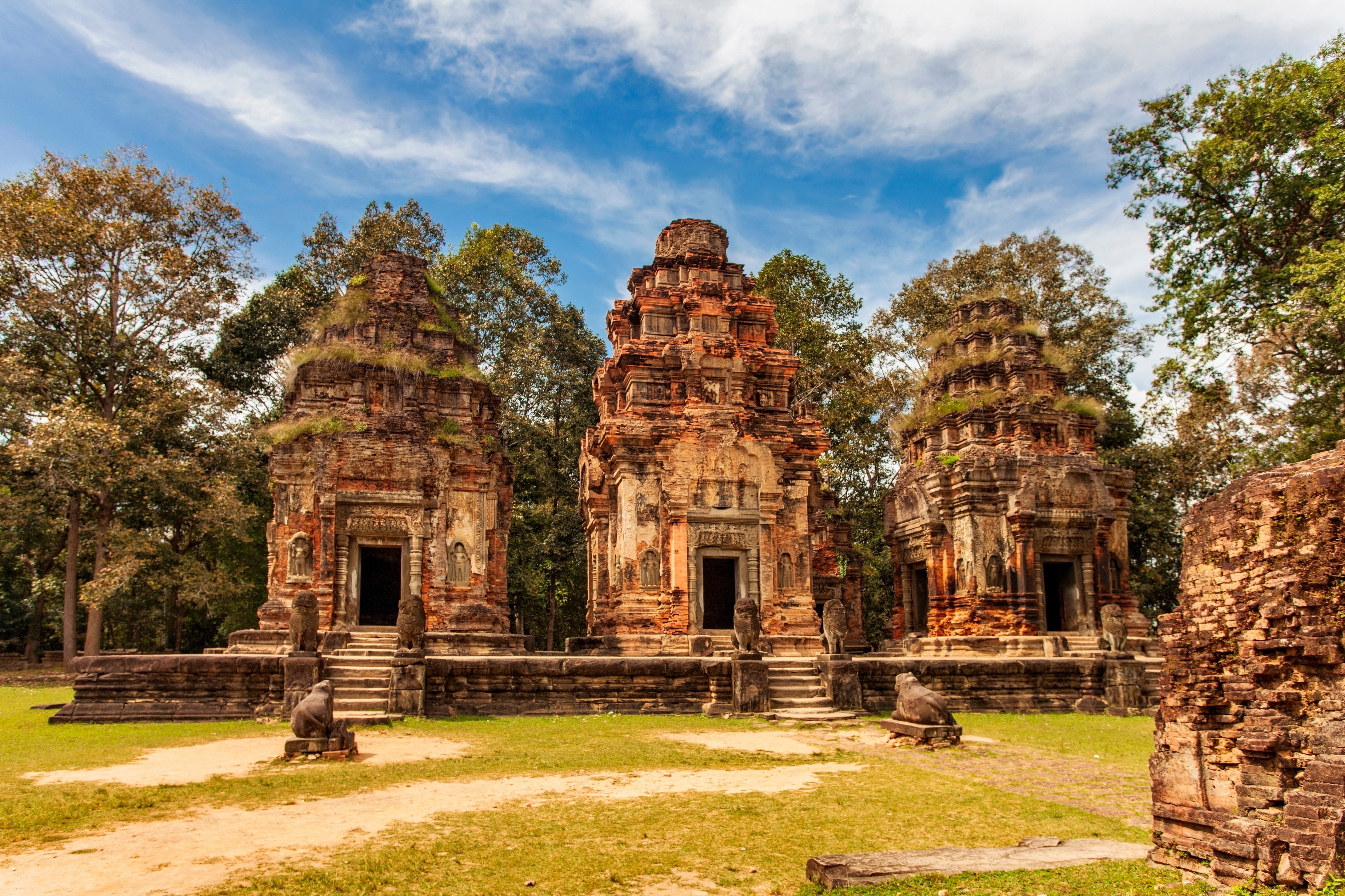 Travel to Cambodia - Ancient Khmer temple ruins in a forest setting, featuring three red sandstone towers with intricate carvings.