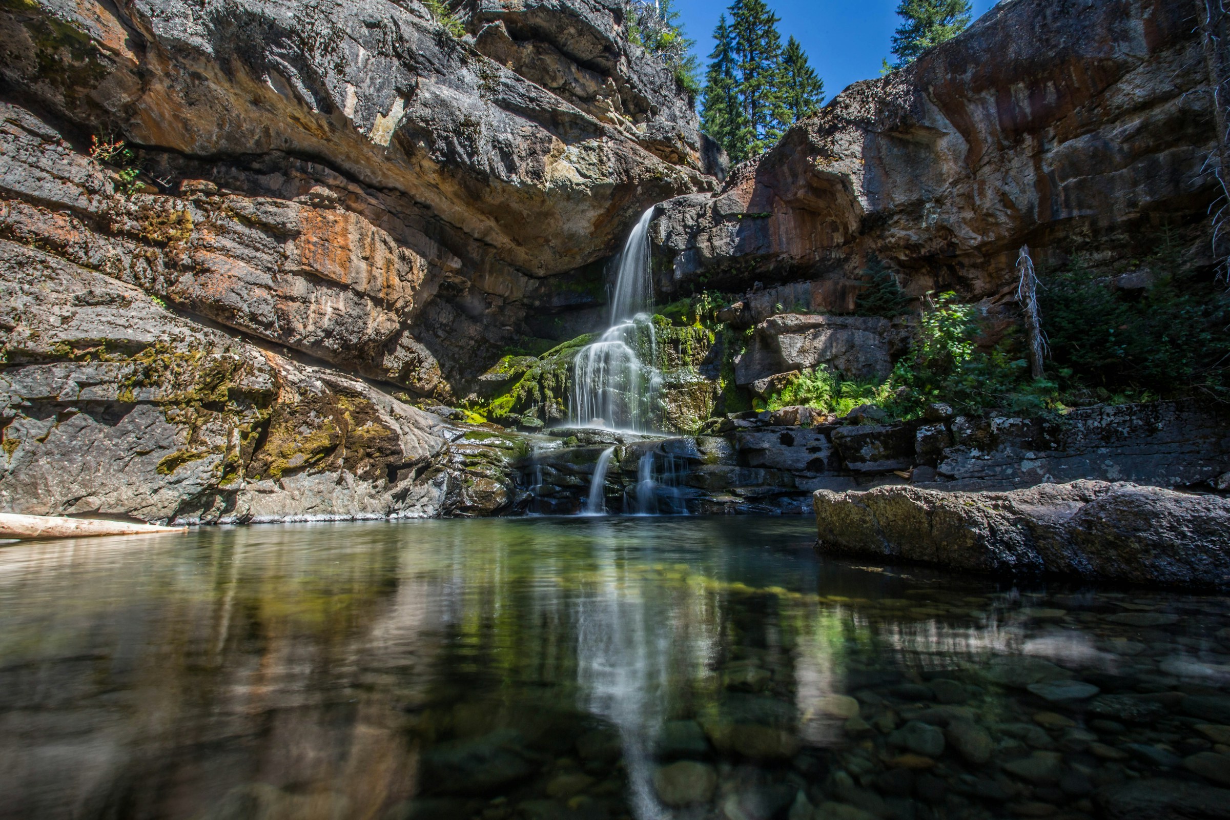 Naturskjønn foss med klart vann og frodige mosegrodde steiner i skogsmiljø.