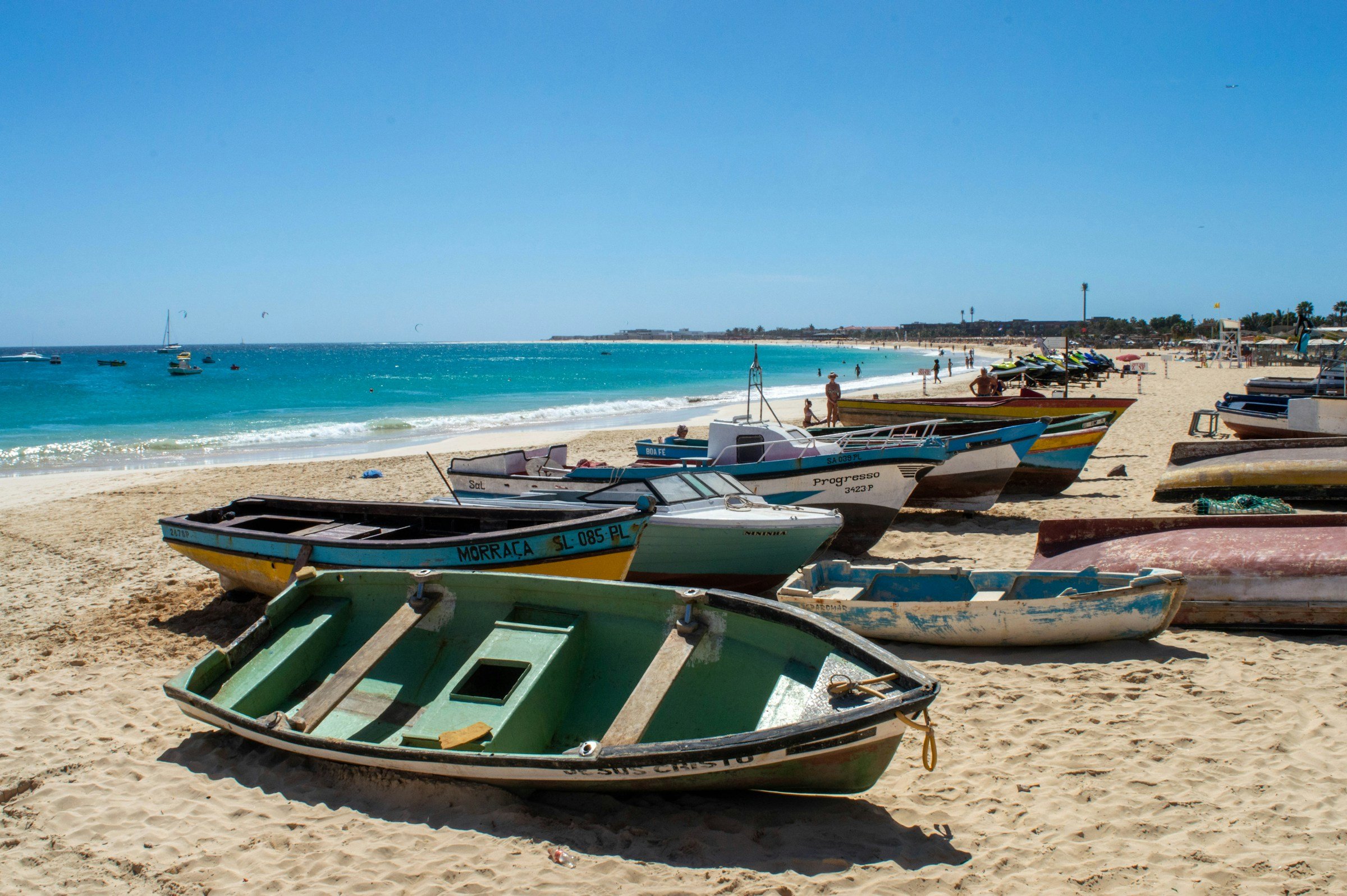 Colorful boats resting on a sandy beach by turquoise ocean waters under a clear blue sky.