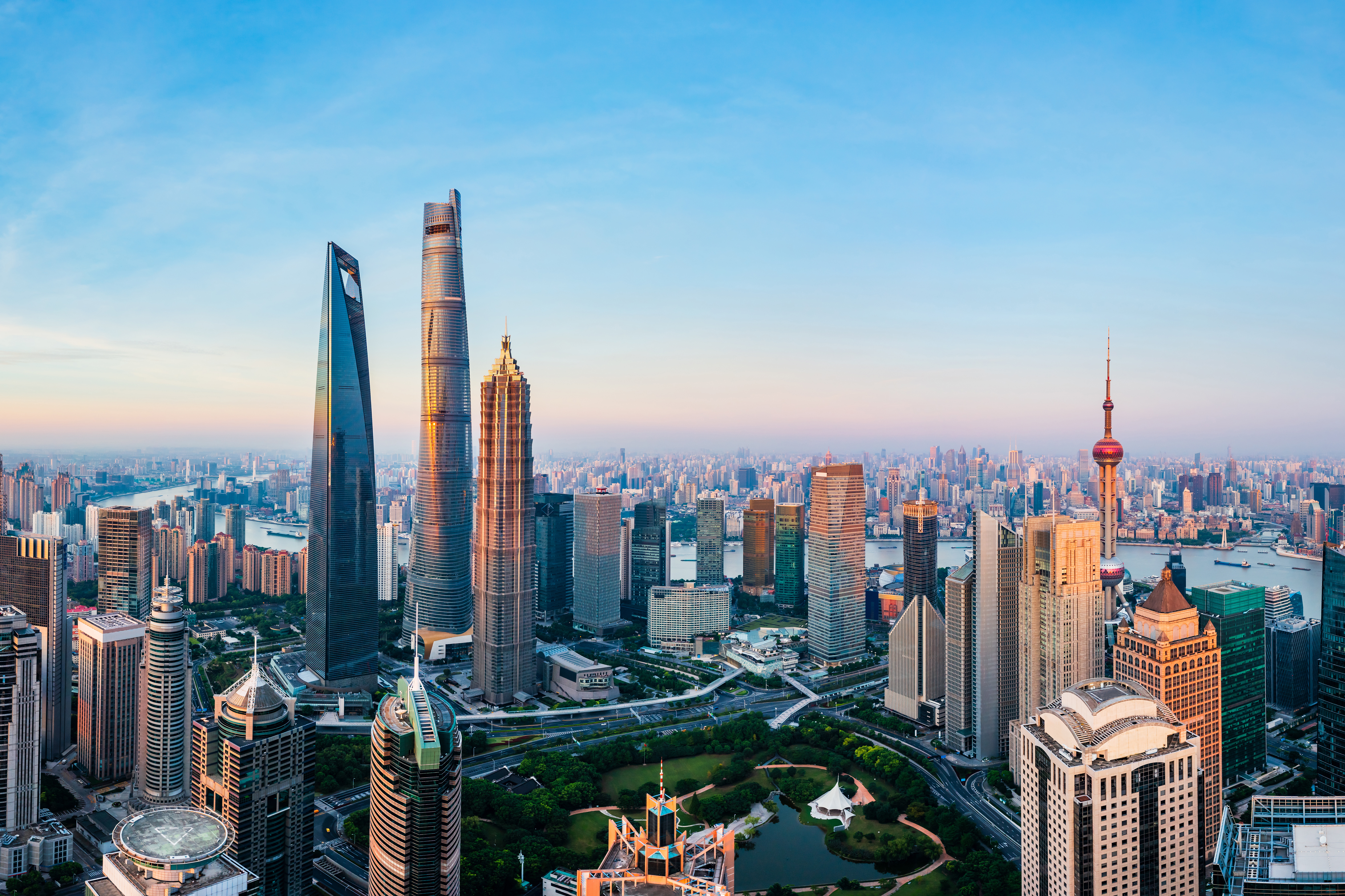 Panoramic view of Shanghai skyline featuring the Shanghai Tower and Oriental Pearl Tower, with skyscrapers and the Huangpu River under a clear blue sky