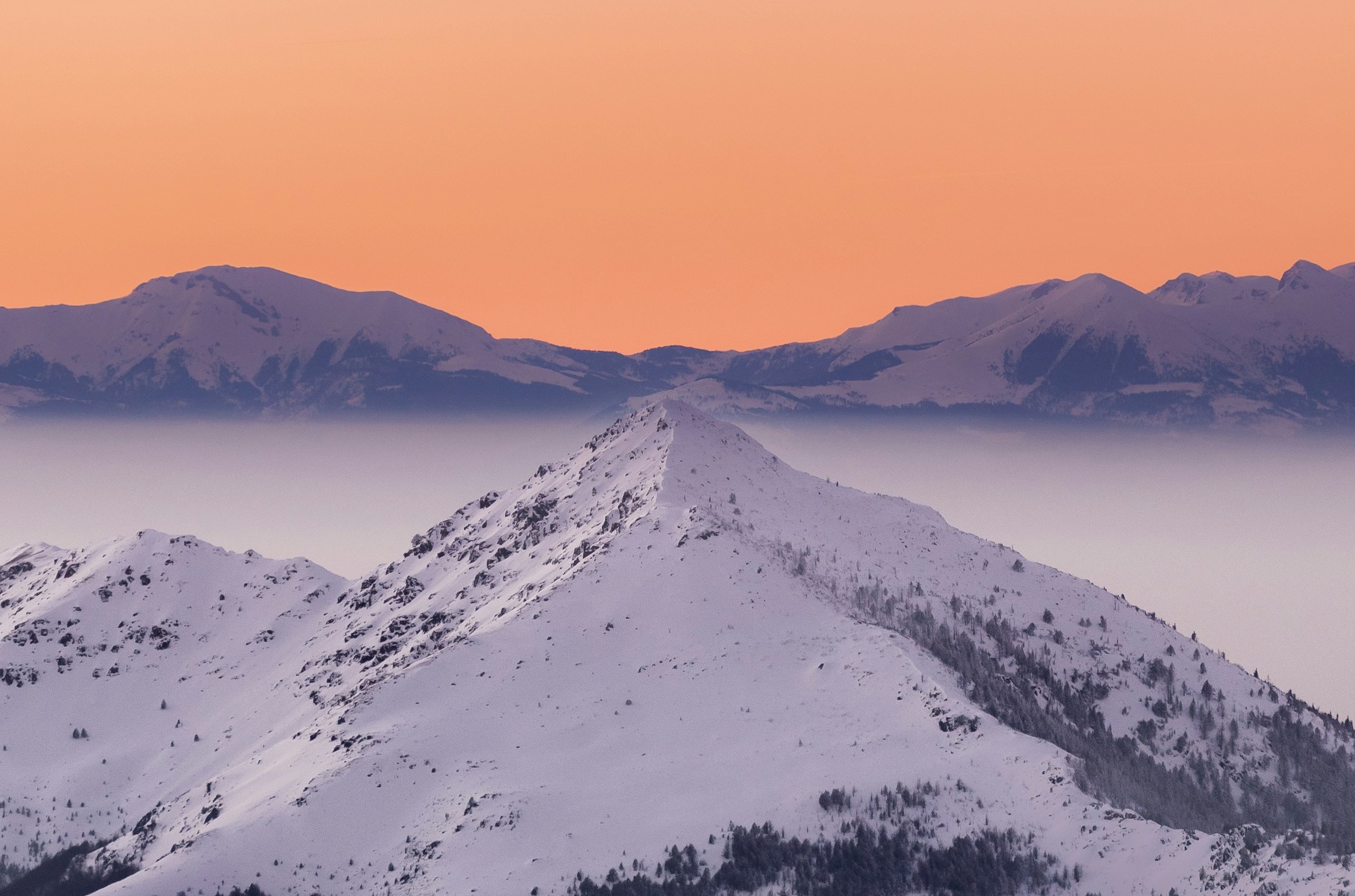 Solnedgang over et fjell og snødekte bakker i Brezovica med en oransje himmel i bakgrunnen