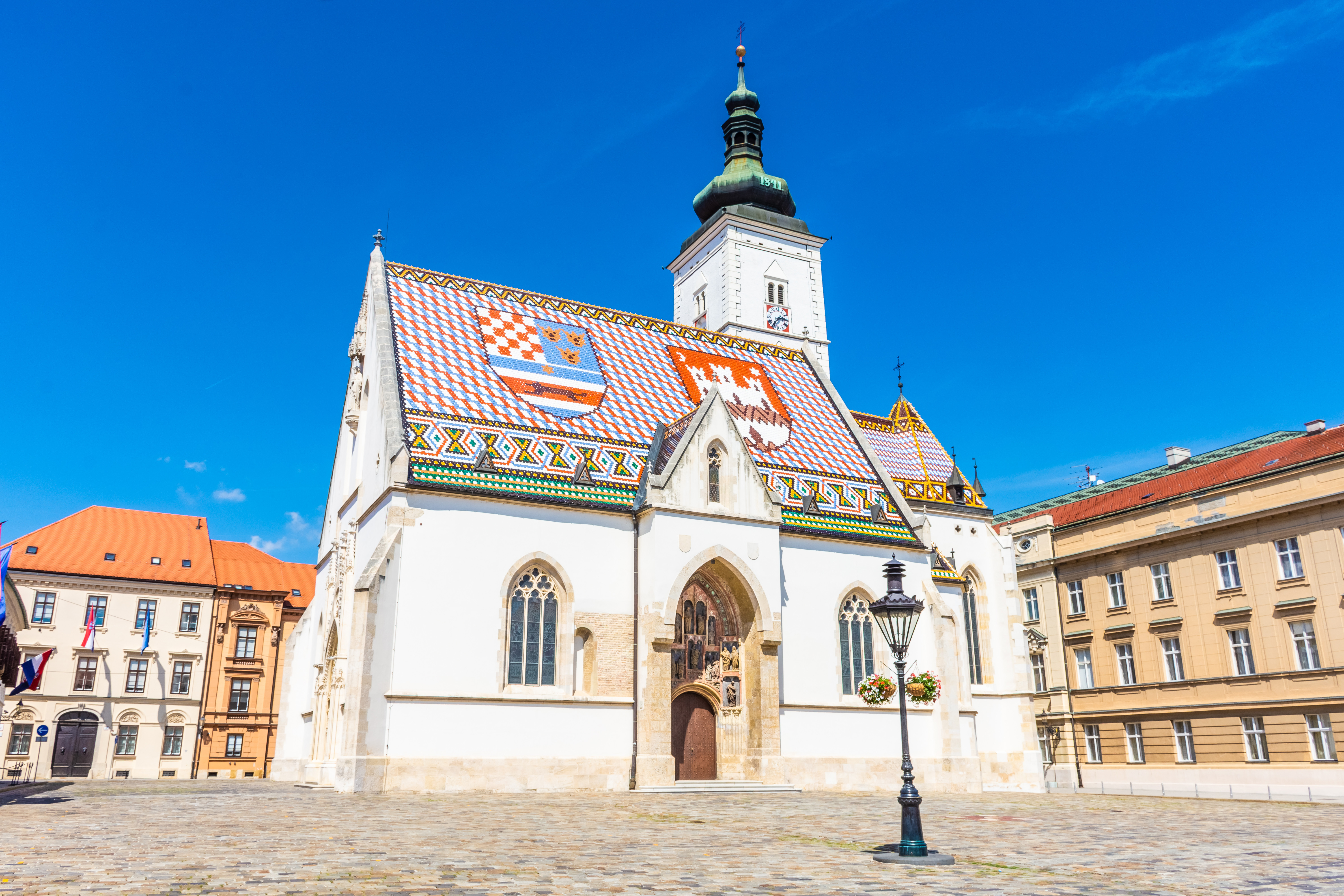 St. Markus' kirke med sitt fargerike tak i Zagreb, Kroatia, under en klar blå himmel. Kalksteinsarkitektur og unike emblemer på taket er fremtredende