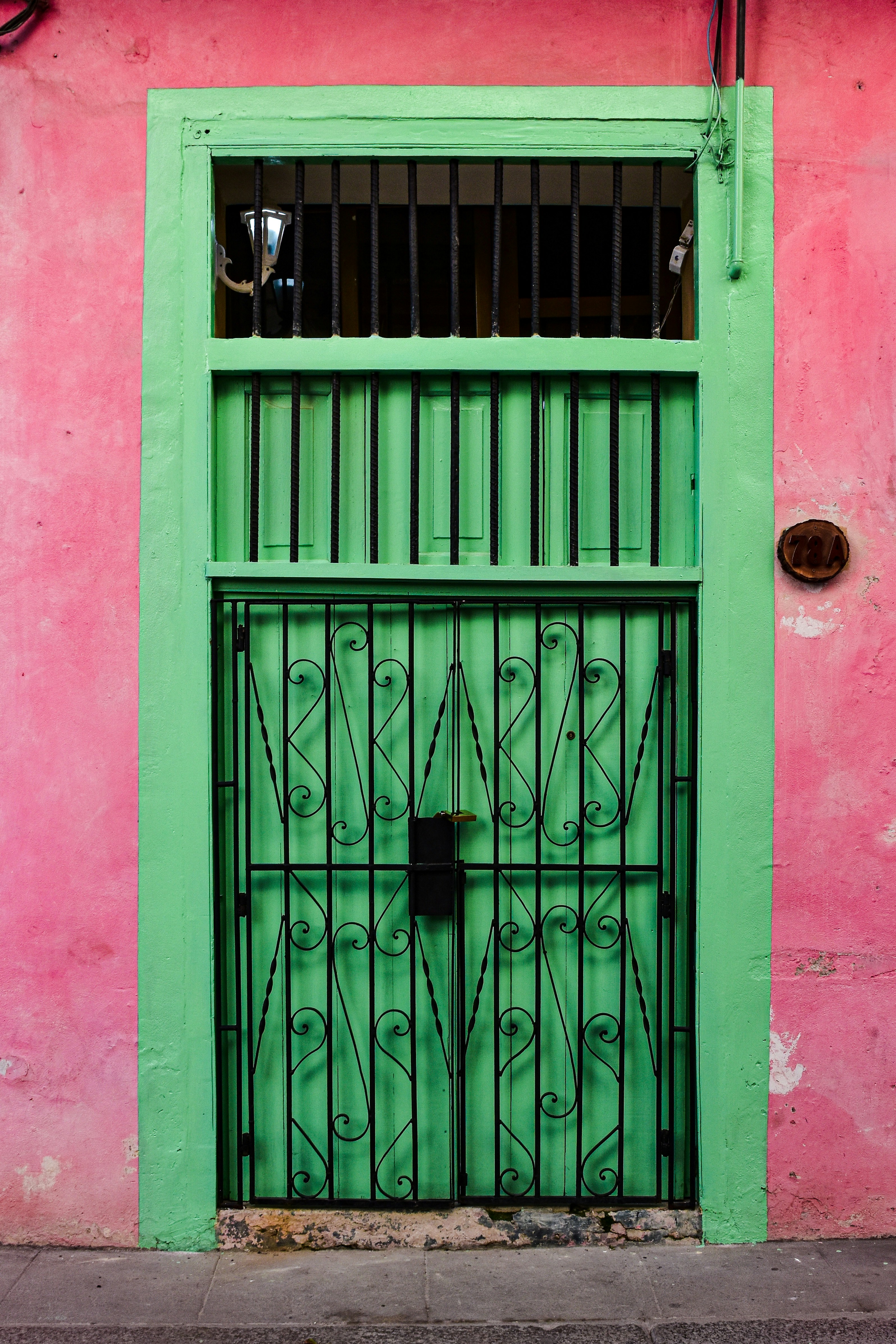 Livlig grønn metalldør med dekorativt svart jernrister, satt mot en fargerik rosa vegg