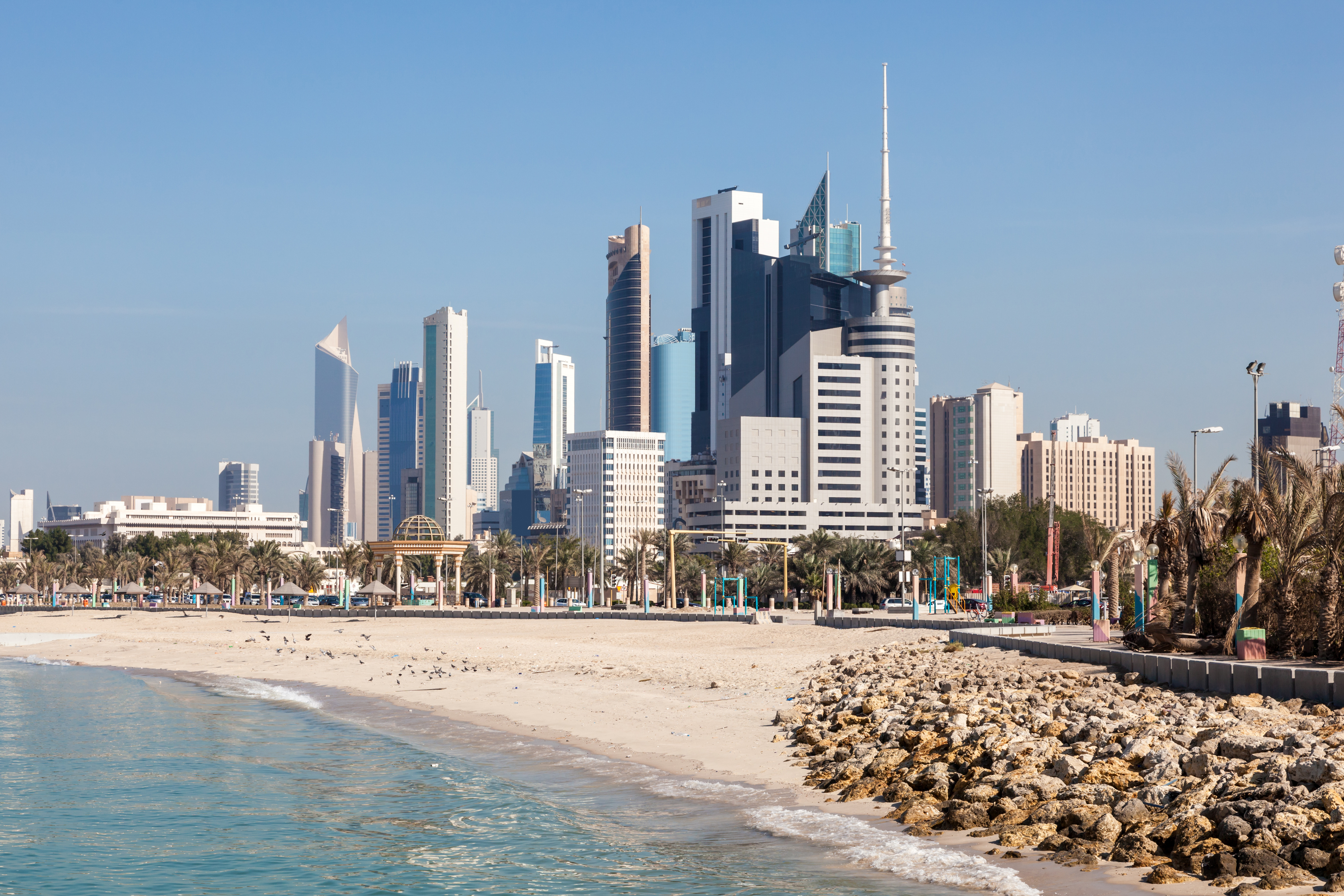 Moderne bysilhuett av Kuwait City med sandstrand og palmer i forgrunnen