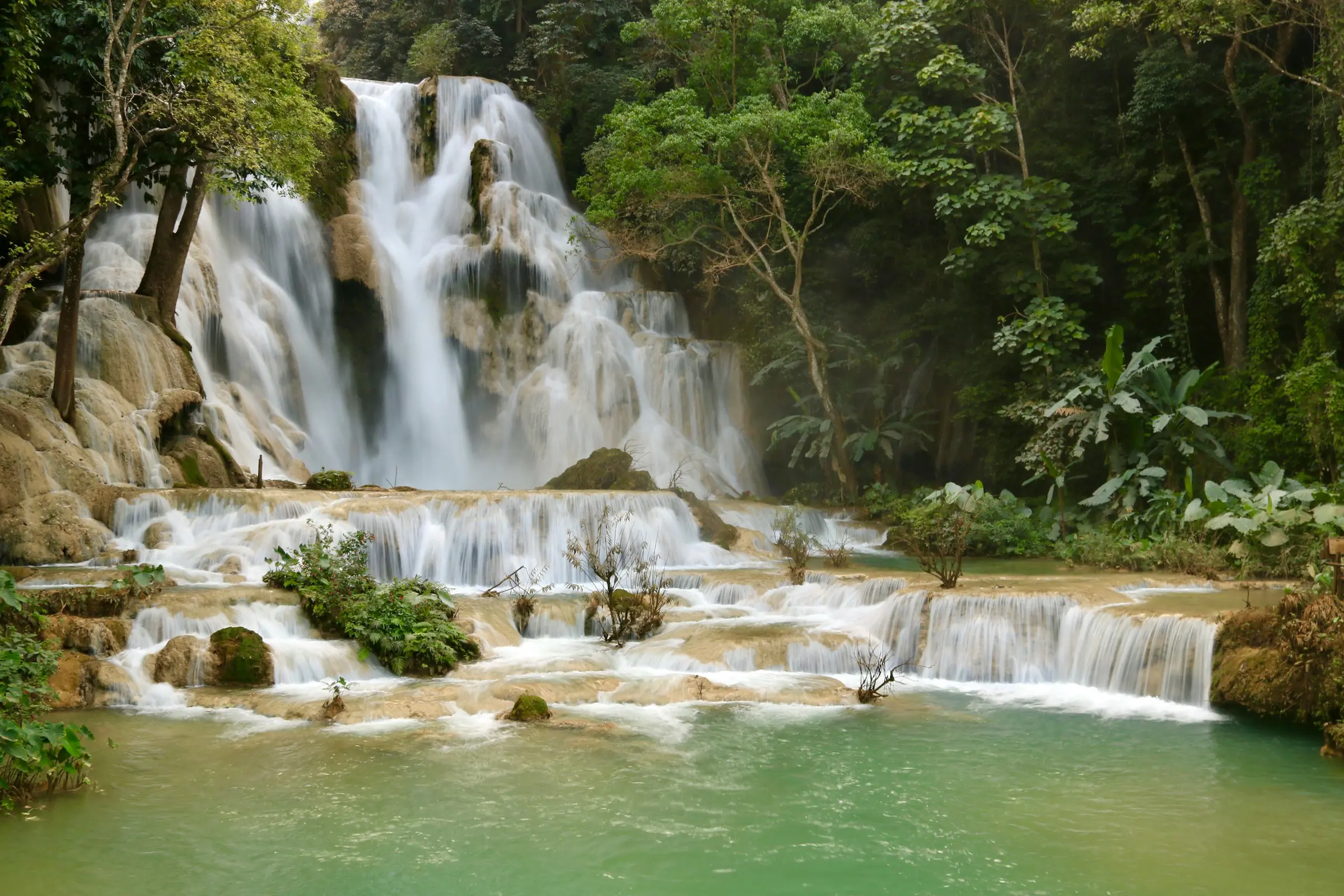 Cascading Kuang Si Waterfalls in lush jungle, turquoise pools surrounded by greenery
