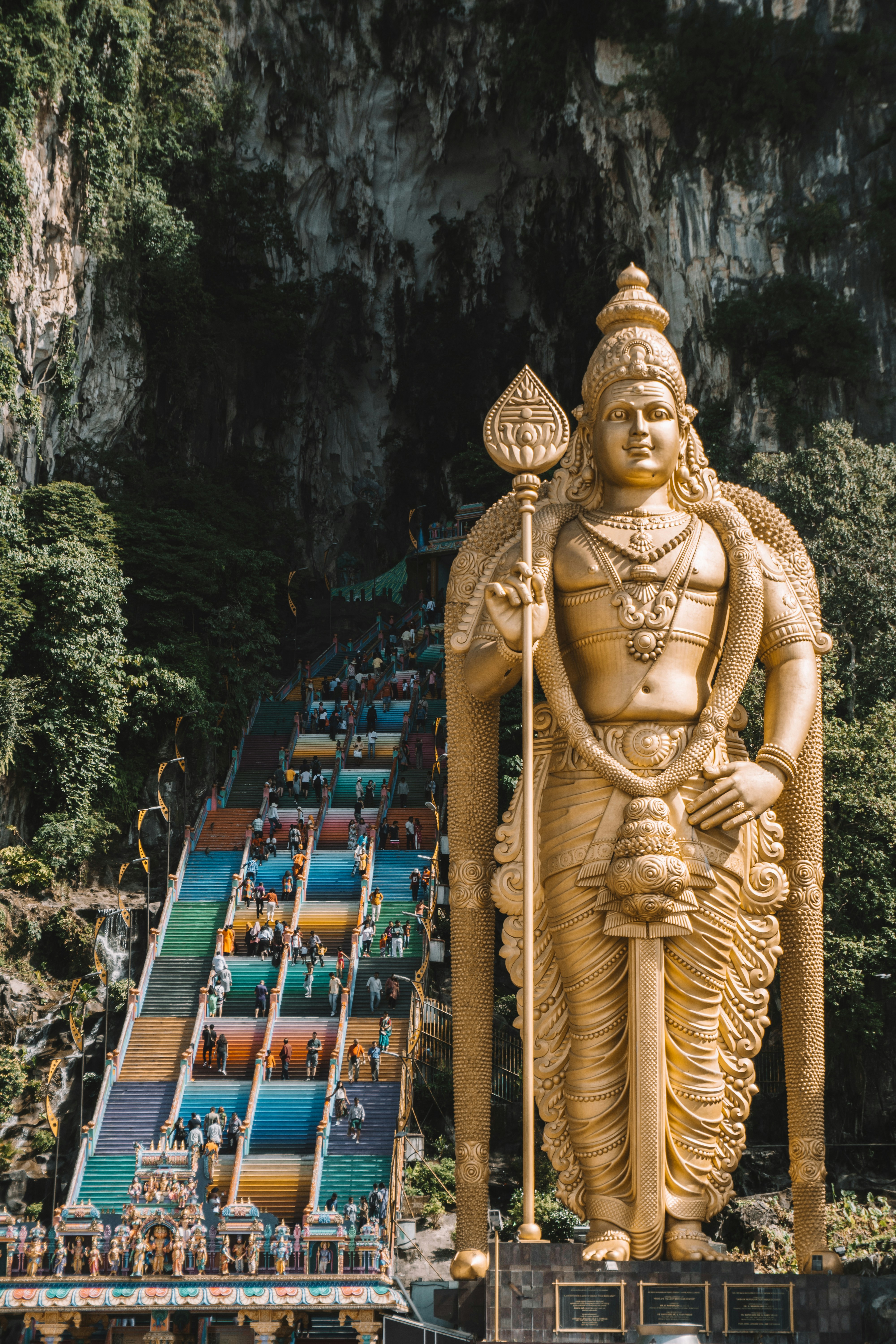 Gyllen statue av Lord Murugan ved inngangen til Batu-hulene i Malaysia, med en fargerik trapp som fører til huletempelet, omgitt av frodige grønne klipper