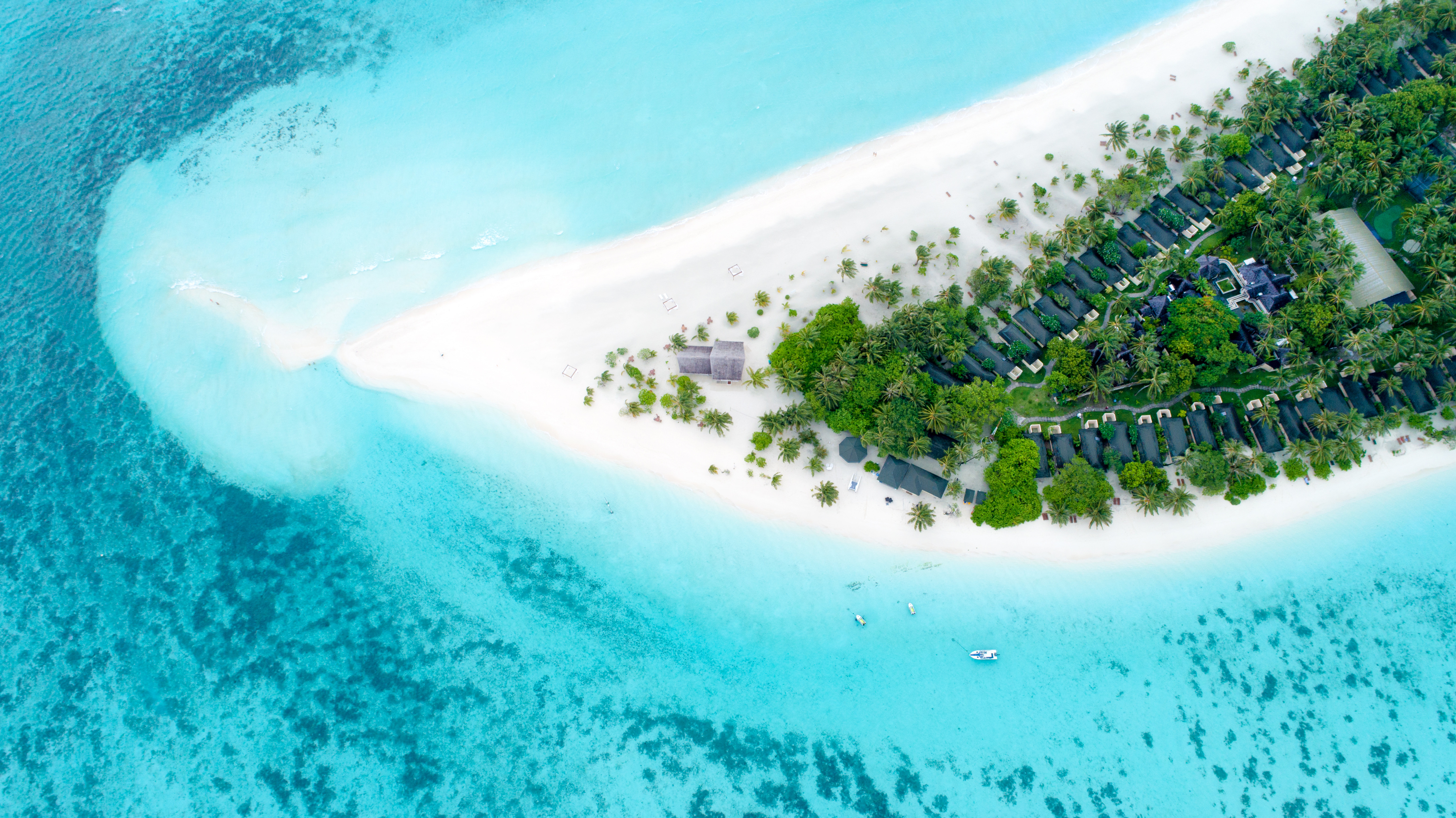 Aerial view of a tropical island with white sandy beaches, clear turquoise waters, lush green vegetation, and waterfront villas