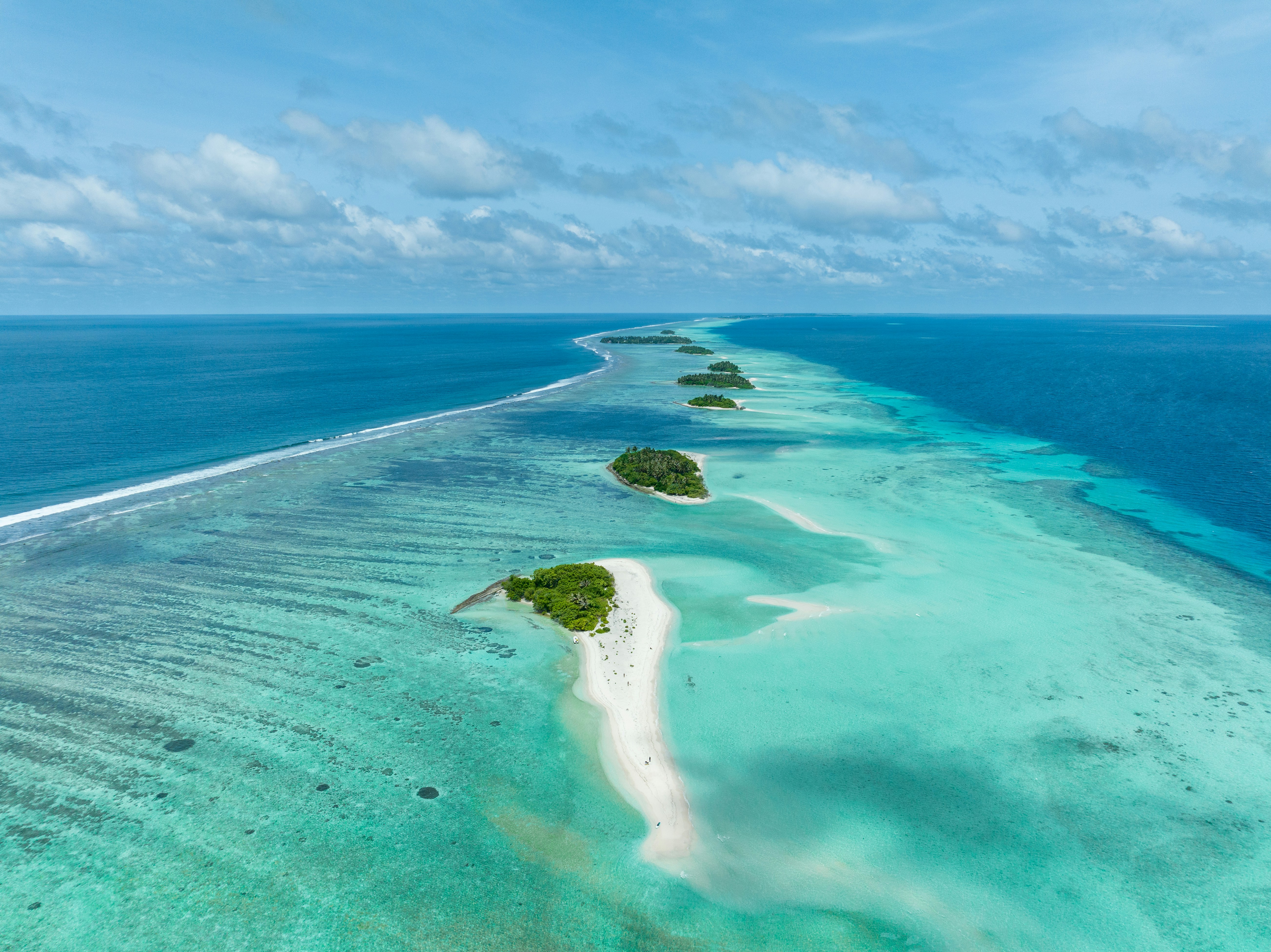 Aerial view of a tropical atoll with lush green islands and white sandy beaches surrounded by turquoise ocean waters under a blue sky