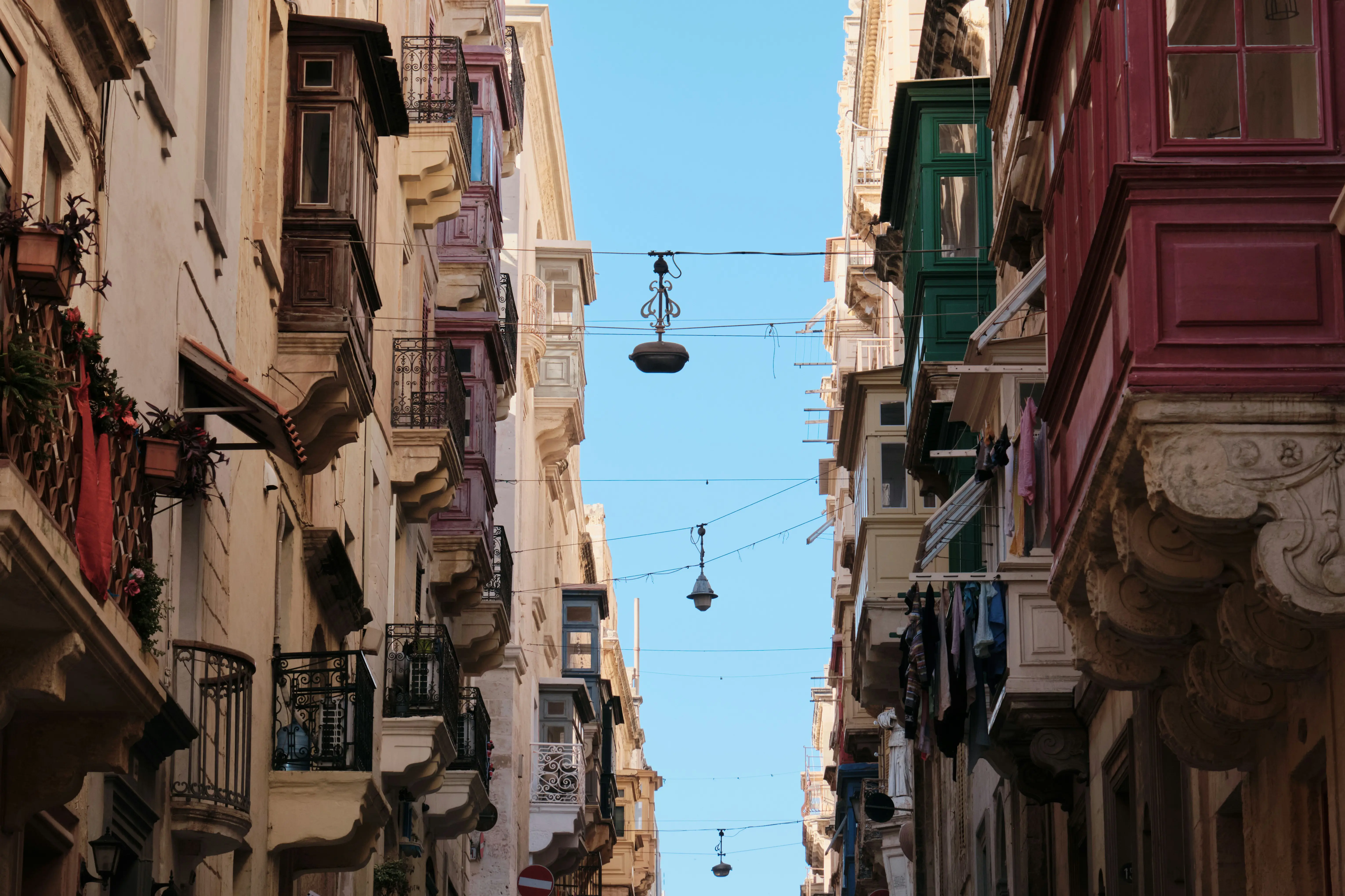 Smal gate med tradisjonelle maltesiske balkonger under en klar blå himmel i Valletta, Malta