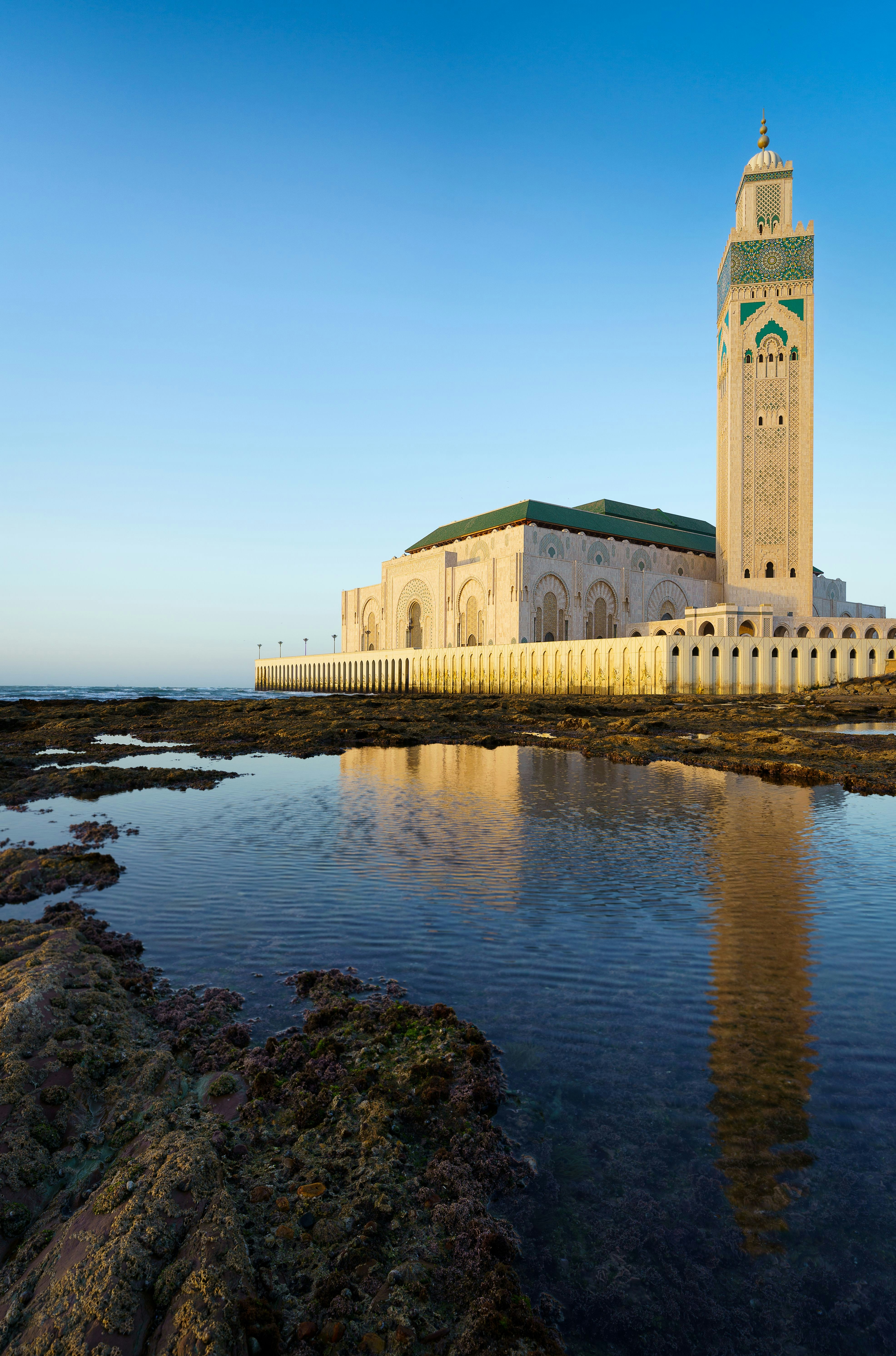 Hassan II-moskeen i Casablanca, Marokko, speilet i rolige kystvann under en klar blå himmel