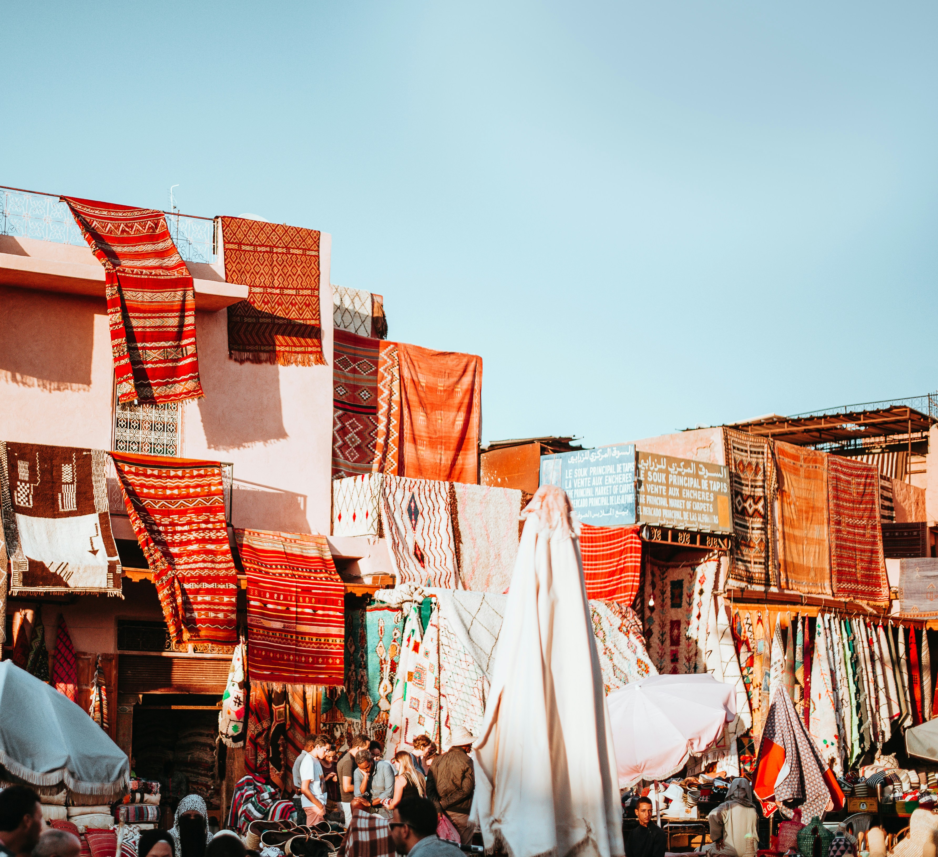 Colorful Moroccan rugs hanging on the walls of a market in Marrakech, showcasing intricate patterns and vibrant hues under a clear blue sky