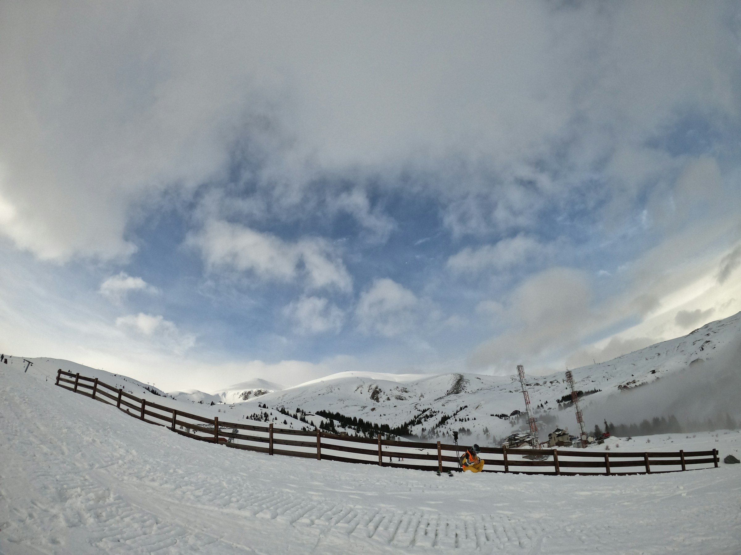 En snødekt skibakke med delvis overskyet himmel og fjell i bakgrunnen