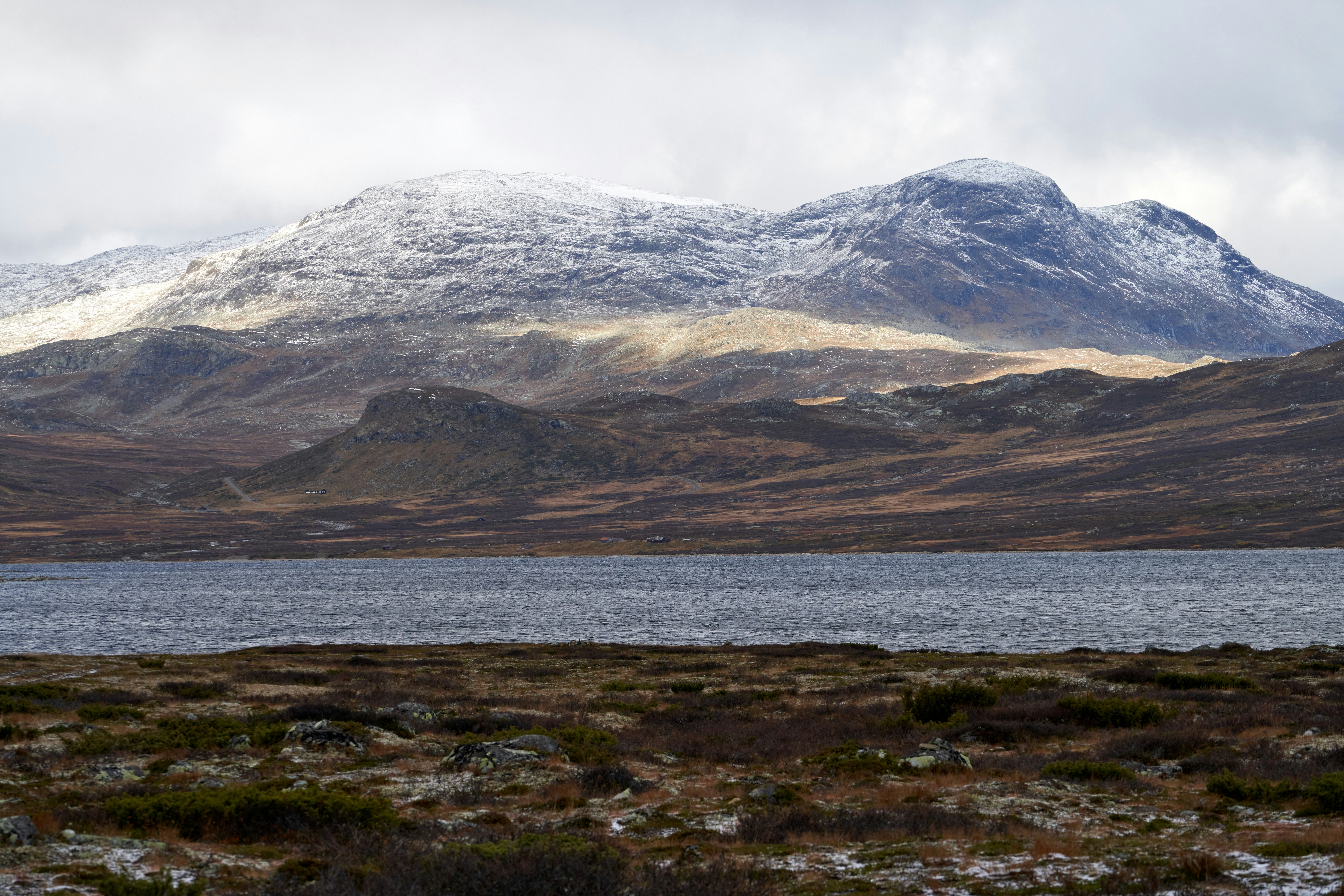 Reis til Hemsedal - Utsikt over elv, fjord og snødekte fjell i Norge med hvit himmel i bakgrunnen