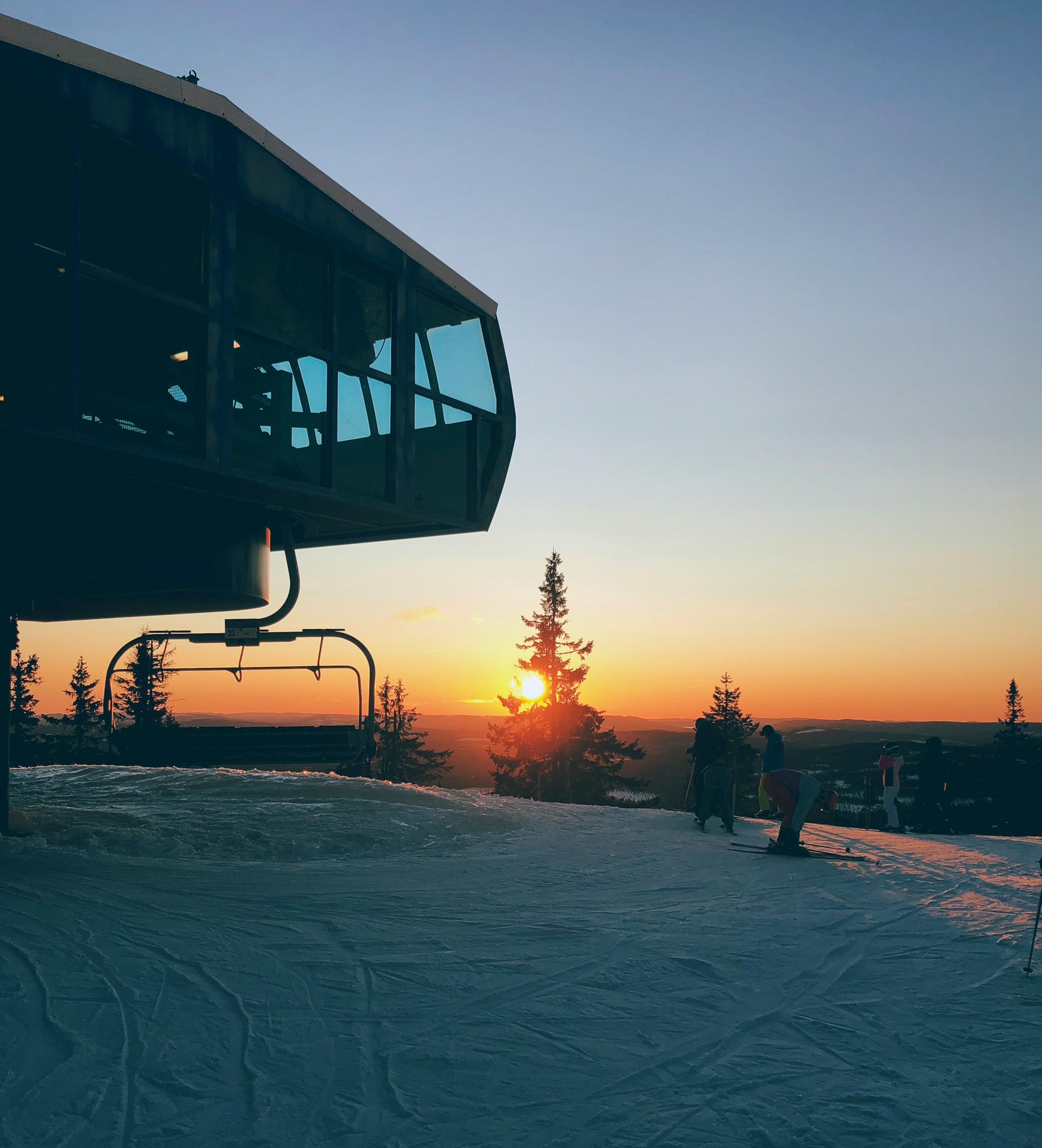 Solnedgang over snødekt landskap i Trysil med skiheis og trær til venstre.