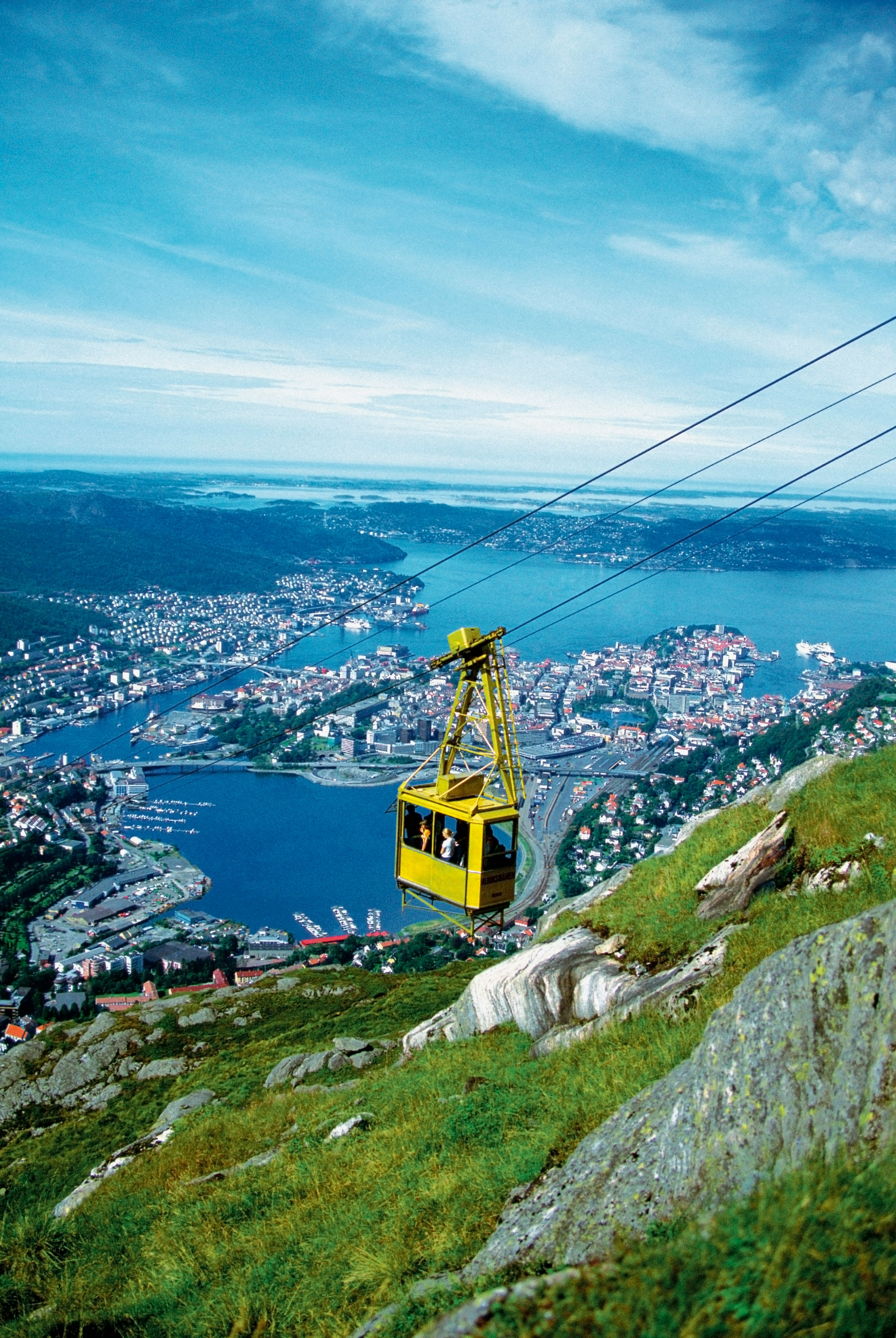 Gul taubane som stiger opp Mount Fløyen med panoramautsikt over Bergen, Norge, inkludert bylandskap og havn under en klar blå himmel