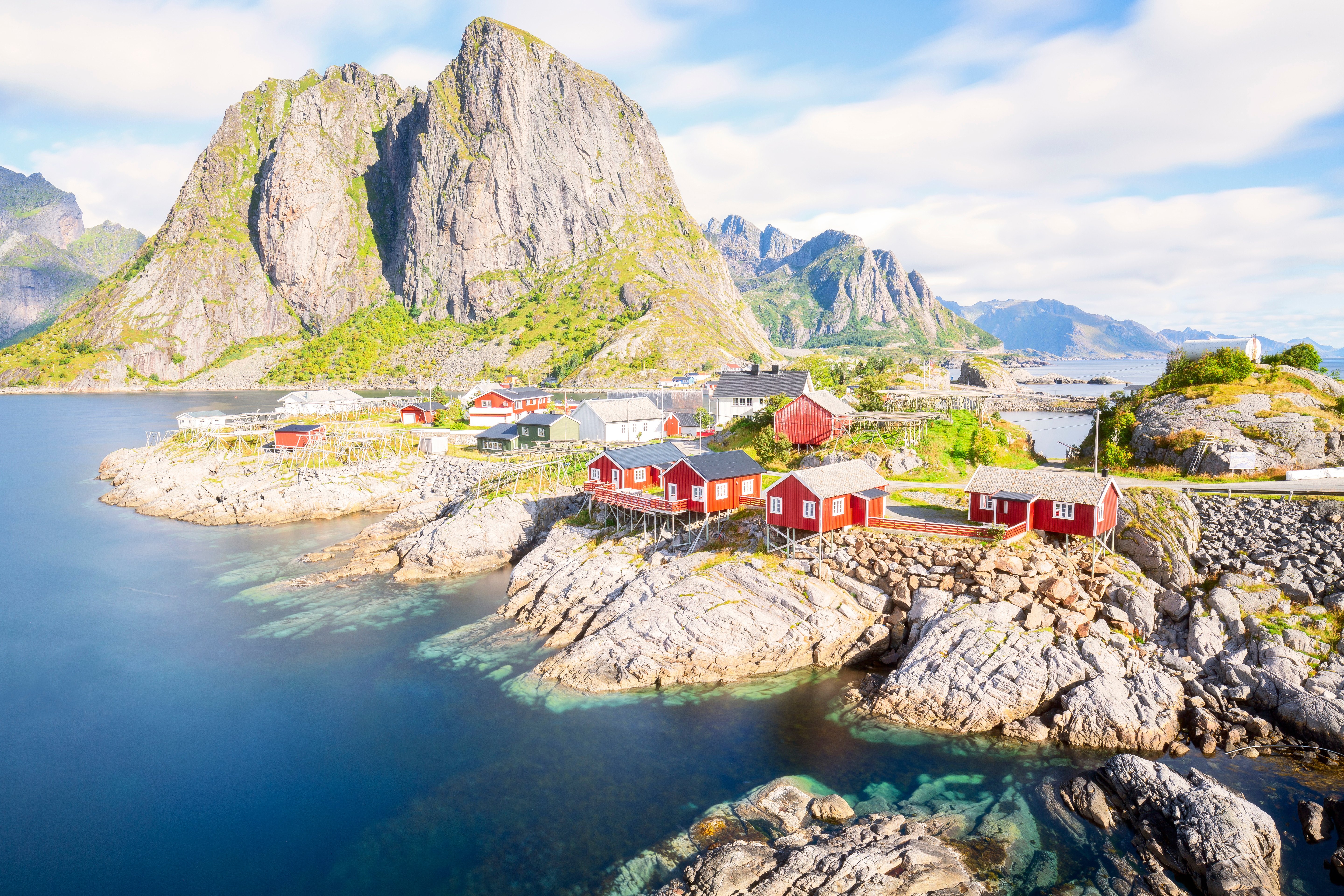 Rorbuer ved kysten i Lofoten, Norge, med fjell i bakgrunnen og klar blå sjø