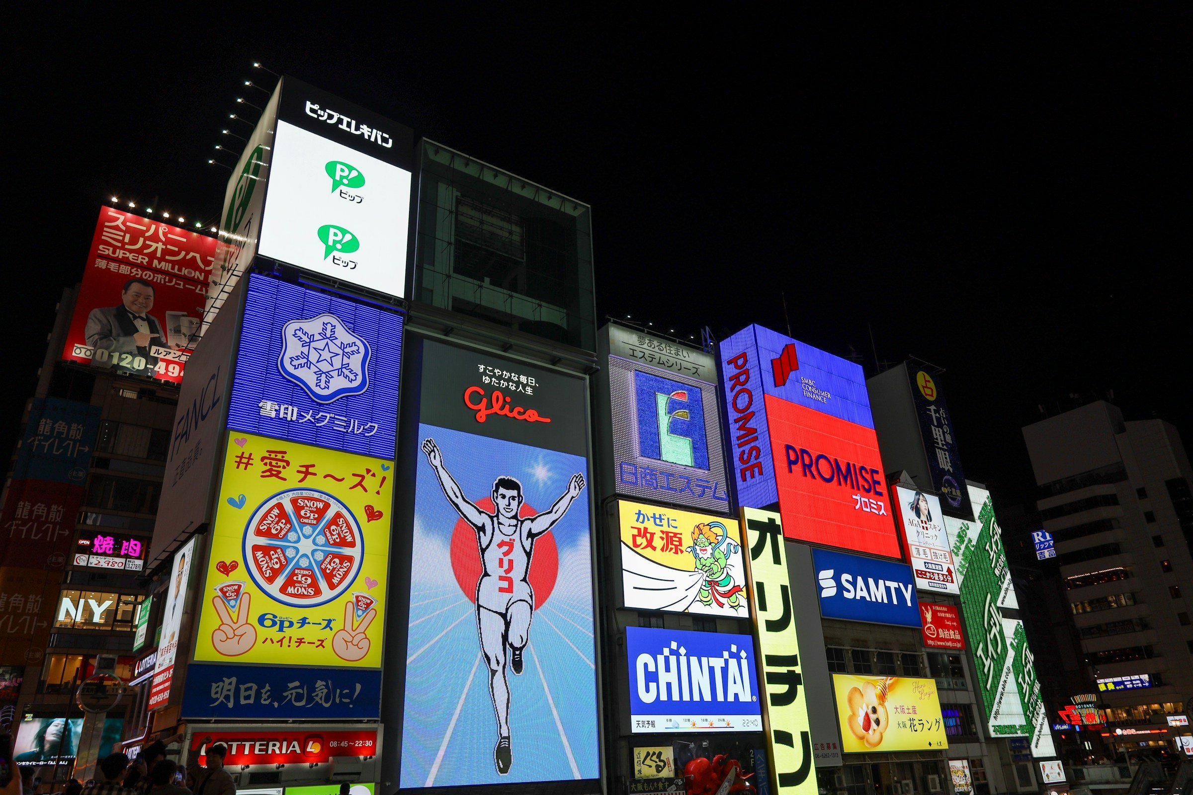 Neonskilt og reklame på bygninger i Dotonbori, Osaka, Japan, med Glica som kjører skilt i midten, nattutsikt.