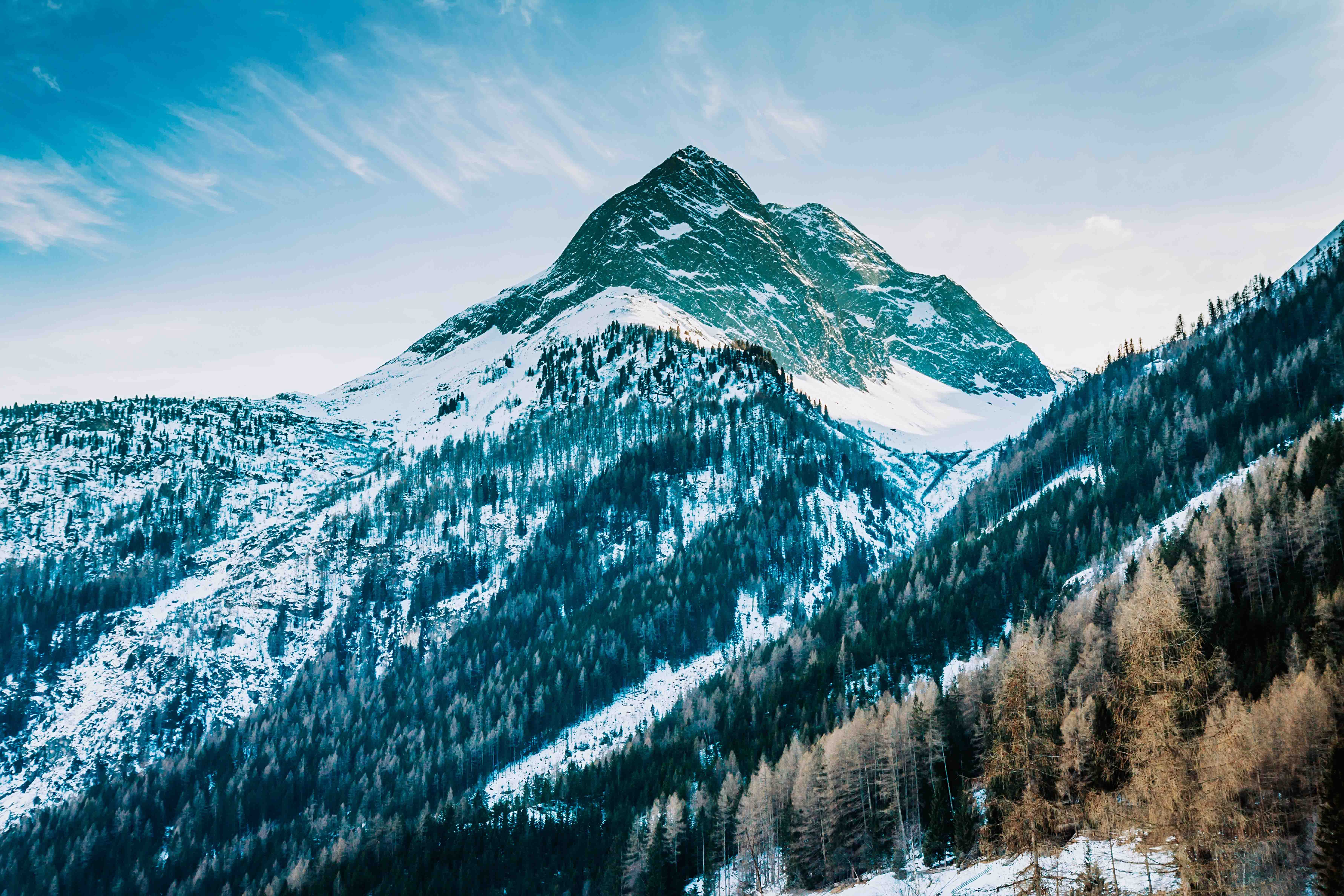 Reis til St. Anton - Snødekt fjelltopp med skogkledde bakker mot en klar blå himmel.
