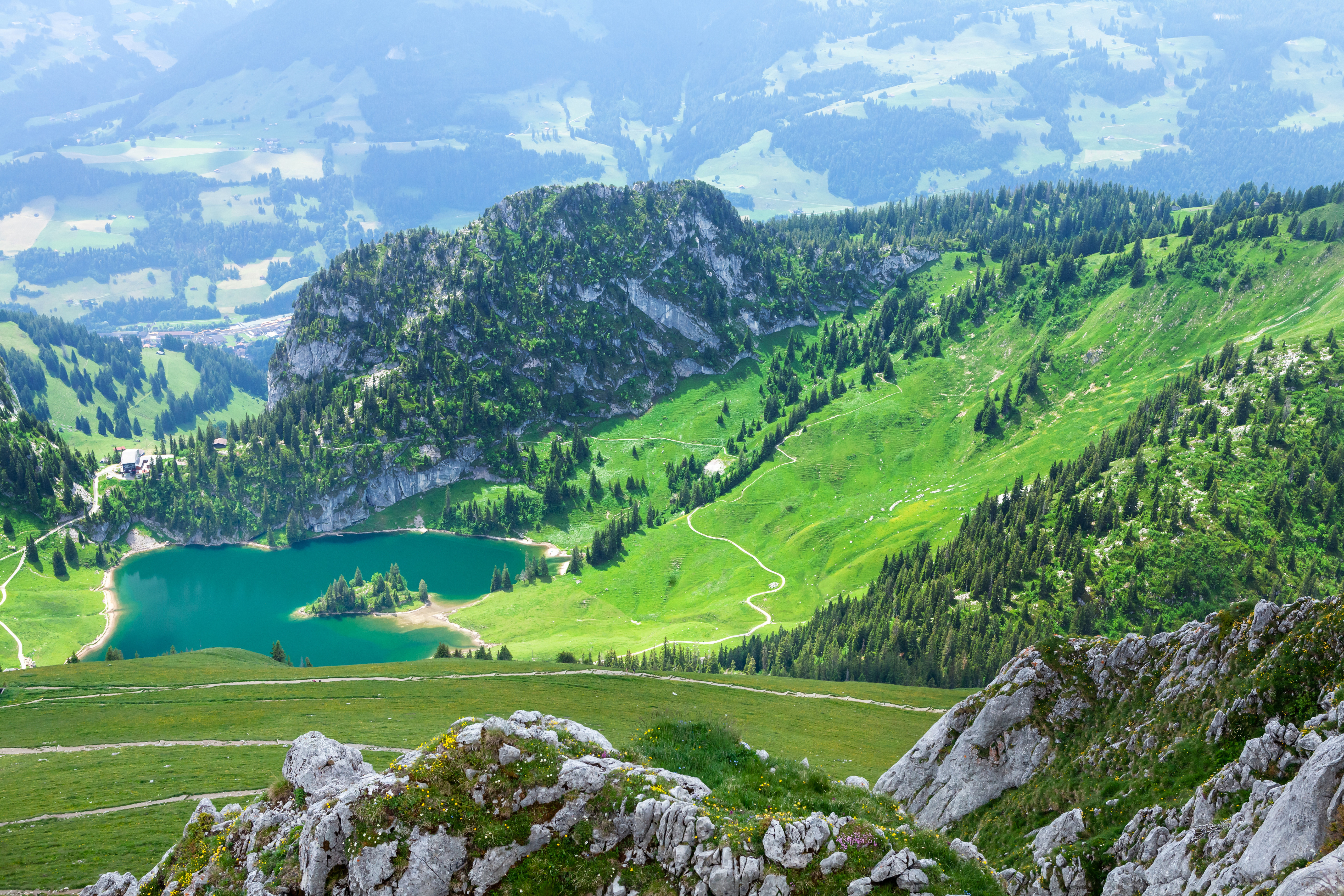 Naturskjønn utsikt over frodige grønne fjell som omgir en klar blå alpesjø, med steinete klipper og svingete stier i en rolig, naturlig omgivelse