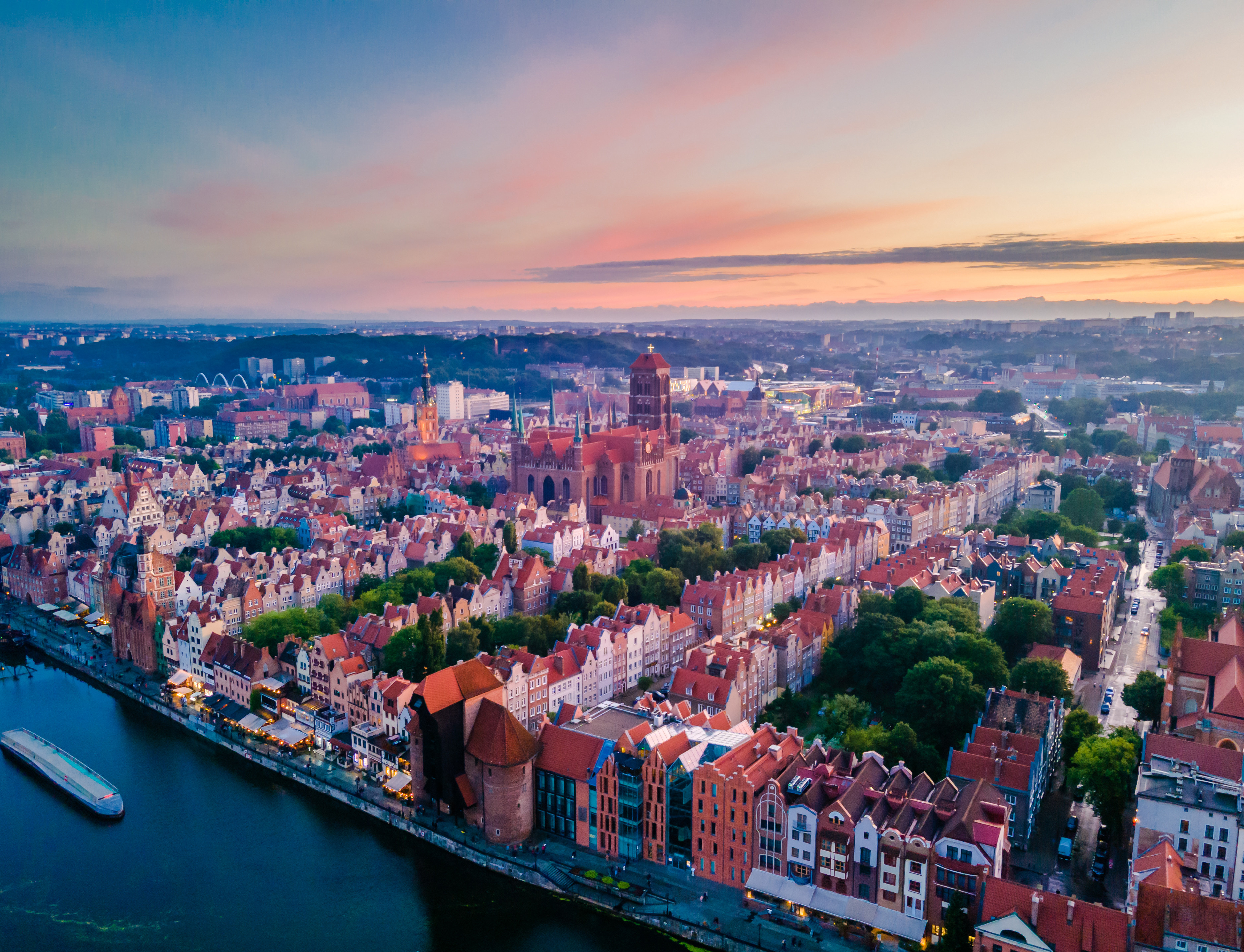 Aerial view of Gdańsk, Poland at sunset, showcasing historic architecture, colorful buildings, and the Motława River with a boat.