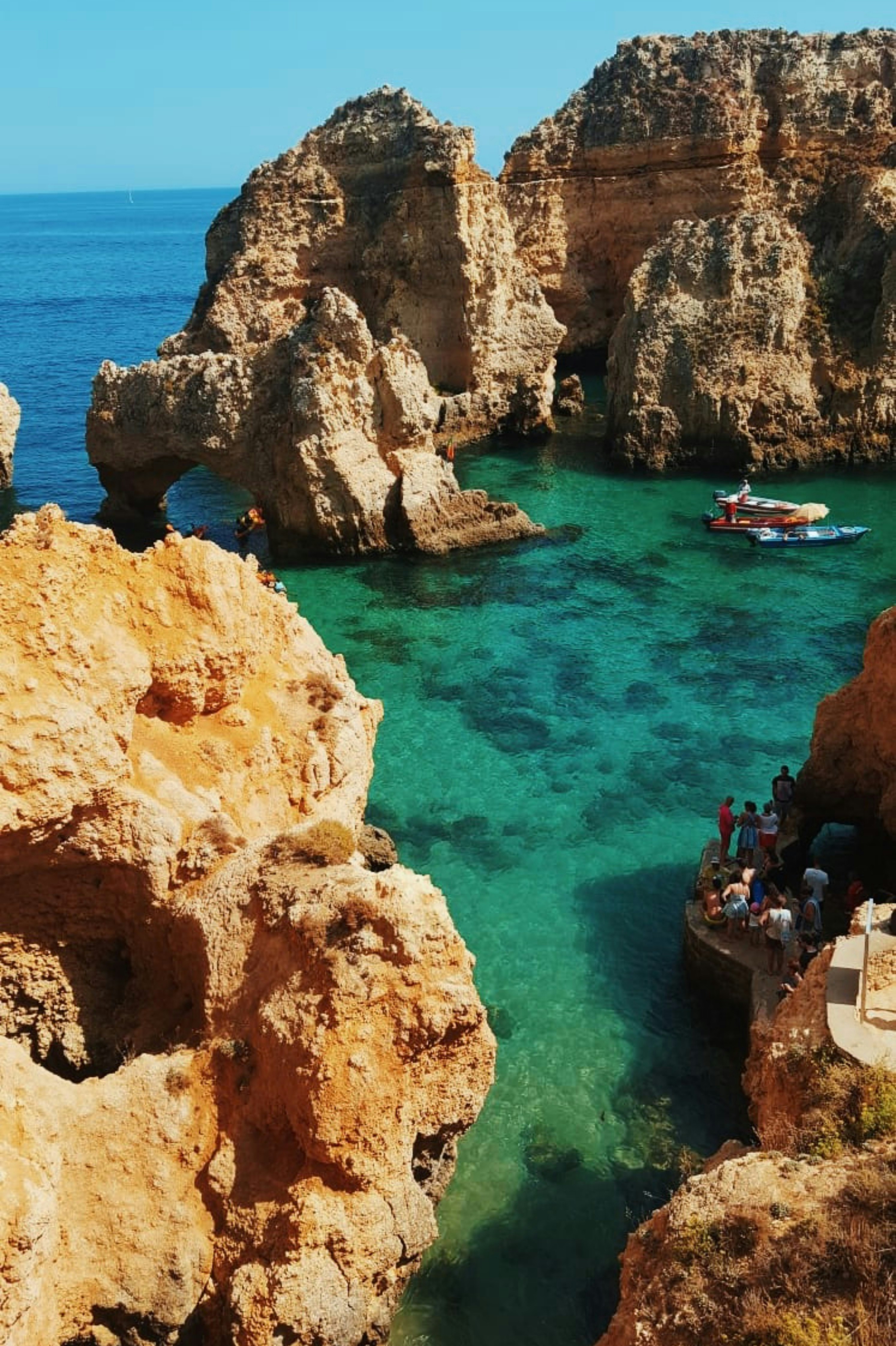 Naturskjønn utsikt over steinete klipper og turkist vann ved Ponta da Piedade, Algarve, Portugal, med en båt og turister som utforsker de naturlige formasjonene
