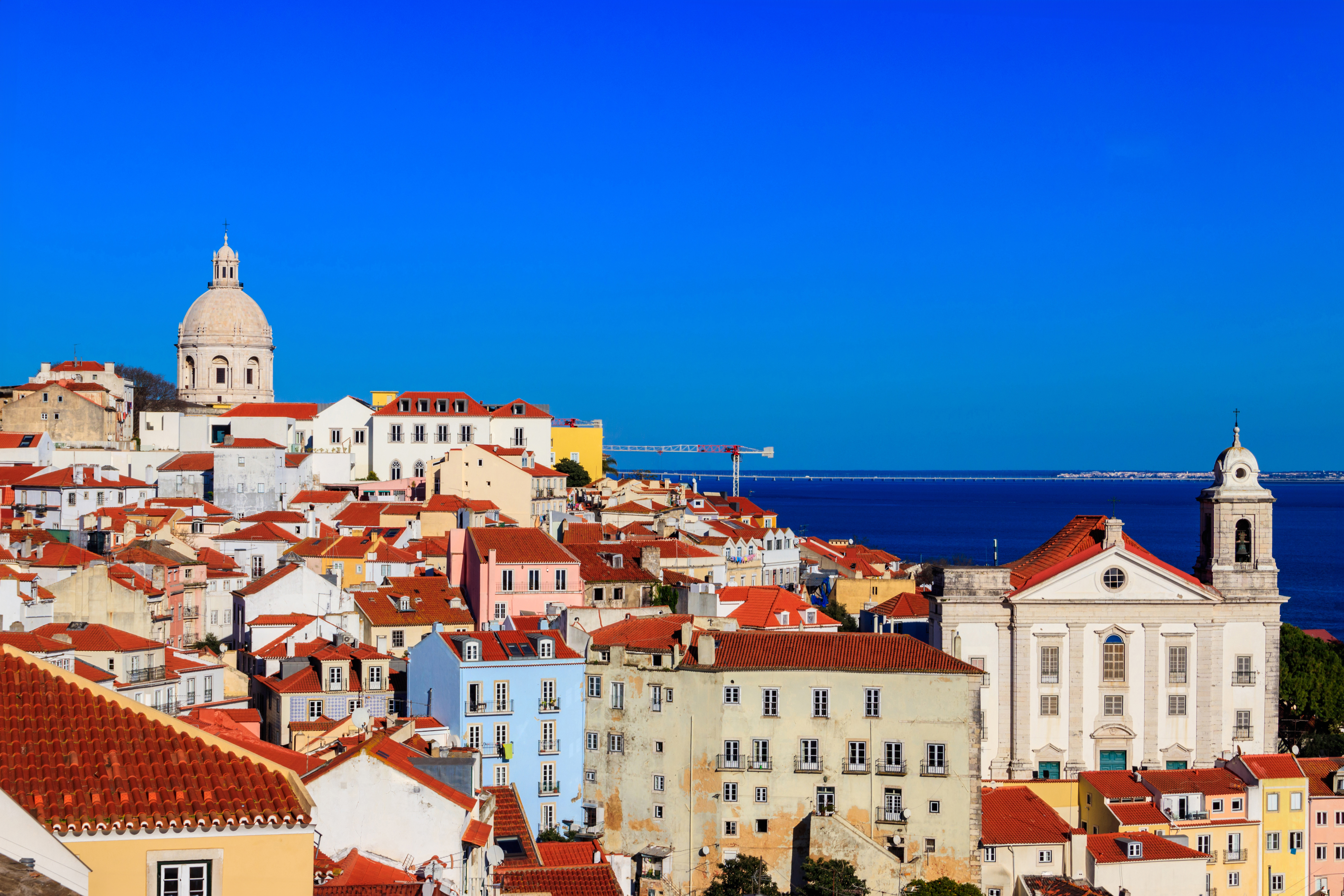 Lisboa bybilde med fargerike hustak og historisk arkitektur, med en klar blå himmel og havet i bakgrunnen