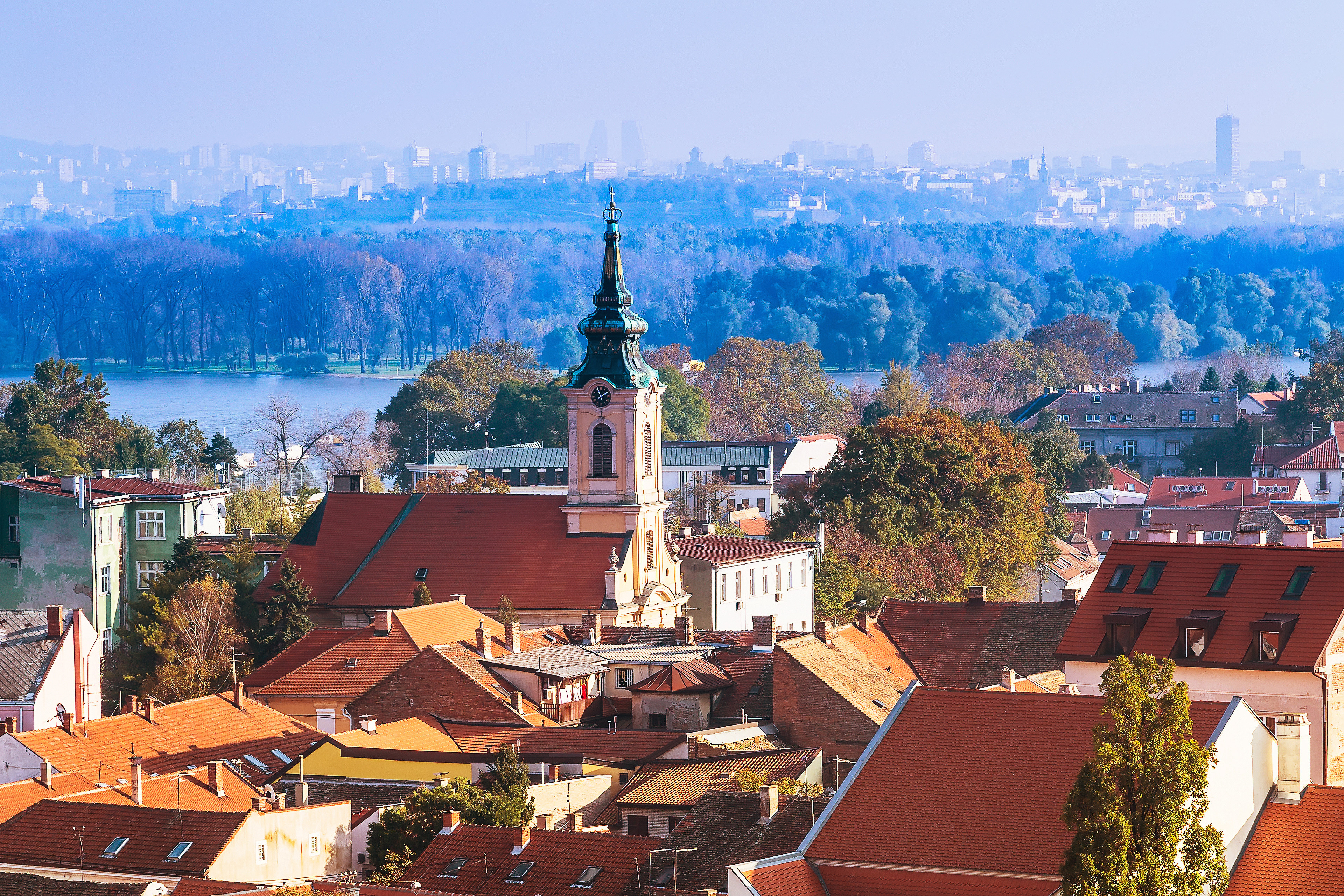 Panoramautsikt over Zemun i Beograd med Sava-elven i bakgrunnen, røde tak, grønn vegetasjon og en kirke med spir dominert av høstfarger