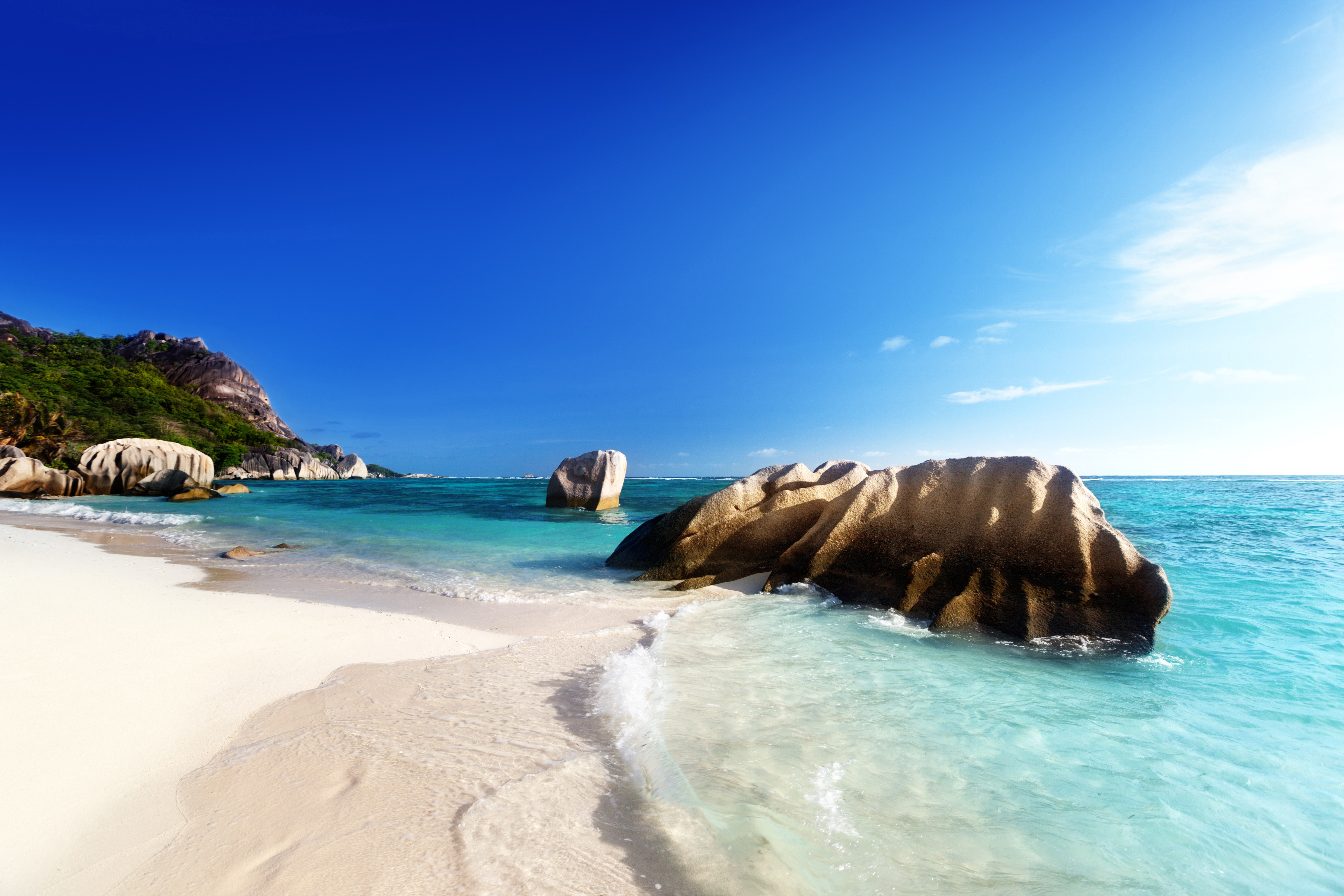 Tropical beach with crystal-clear turquoise water, granite boulders, and white sand under a bright blue sky