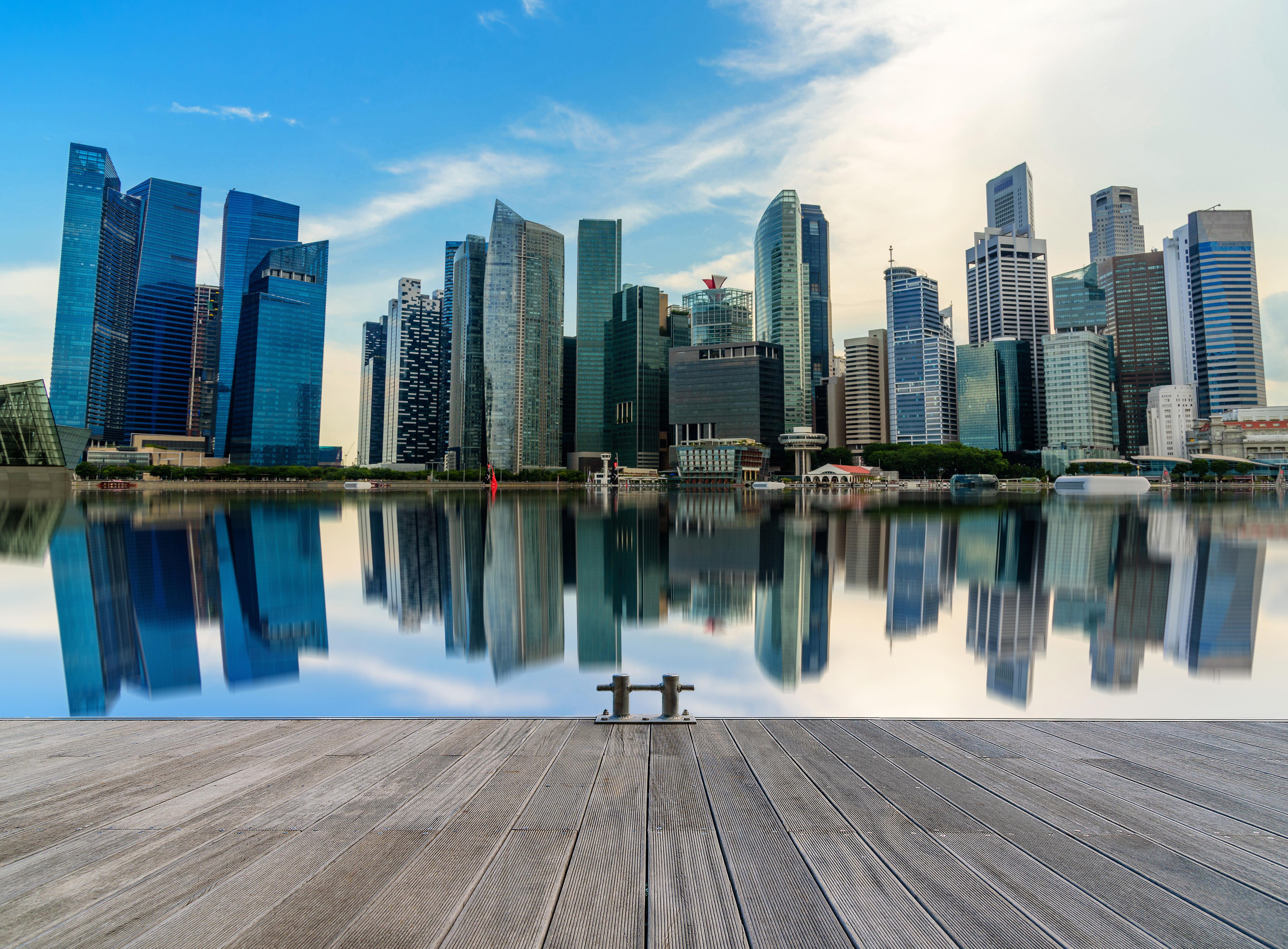 Moderne Singapore-skyline med ruvende skyskrapere som speiler seg i vannet, sett fra en treterrasse på en klar dag