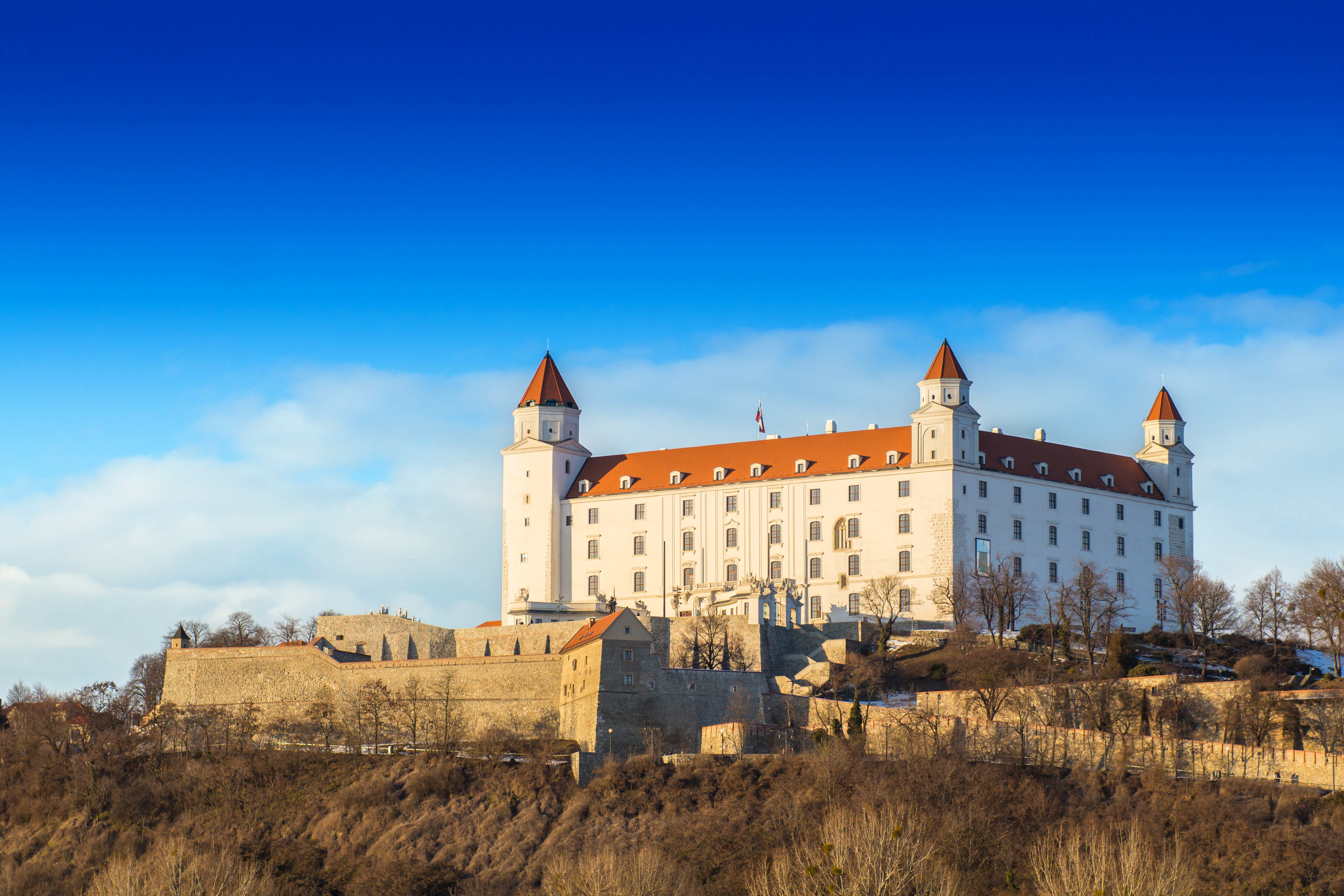 Bratislava slott på en solfylt dag, med sitt karakteristiske røde tak og hvite fasade, mot en klar blå himmel