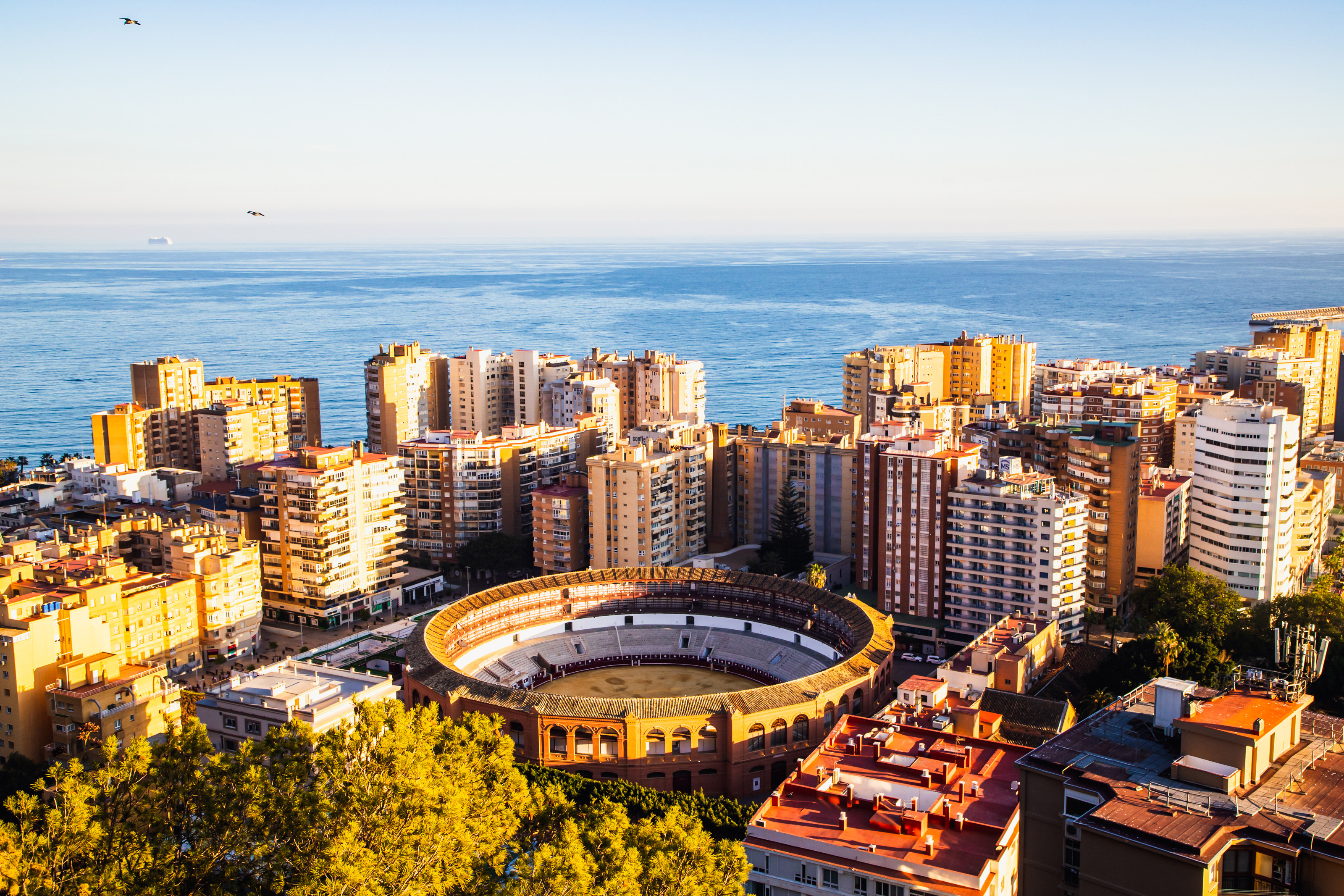 Aerial view of the Malagueta bullring surrounded by modern buildings in the vibrant city of Málaga, Spain, with the Mediterranean Sea in the background