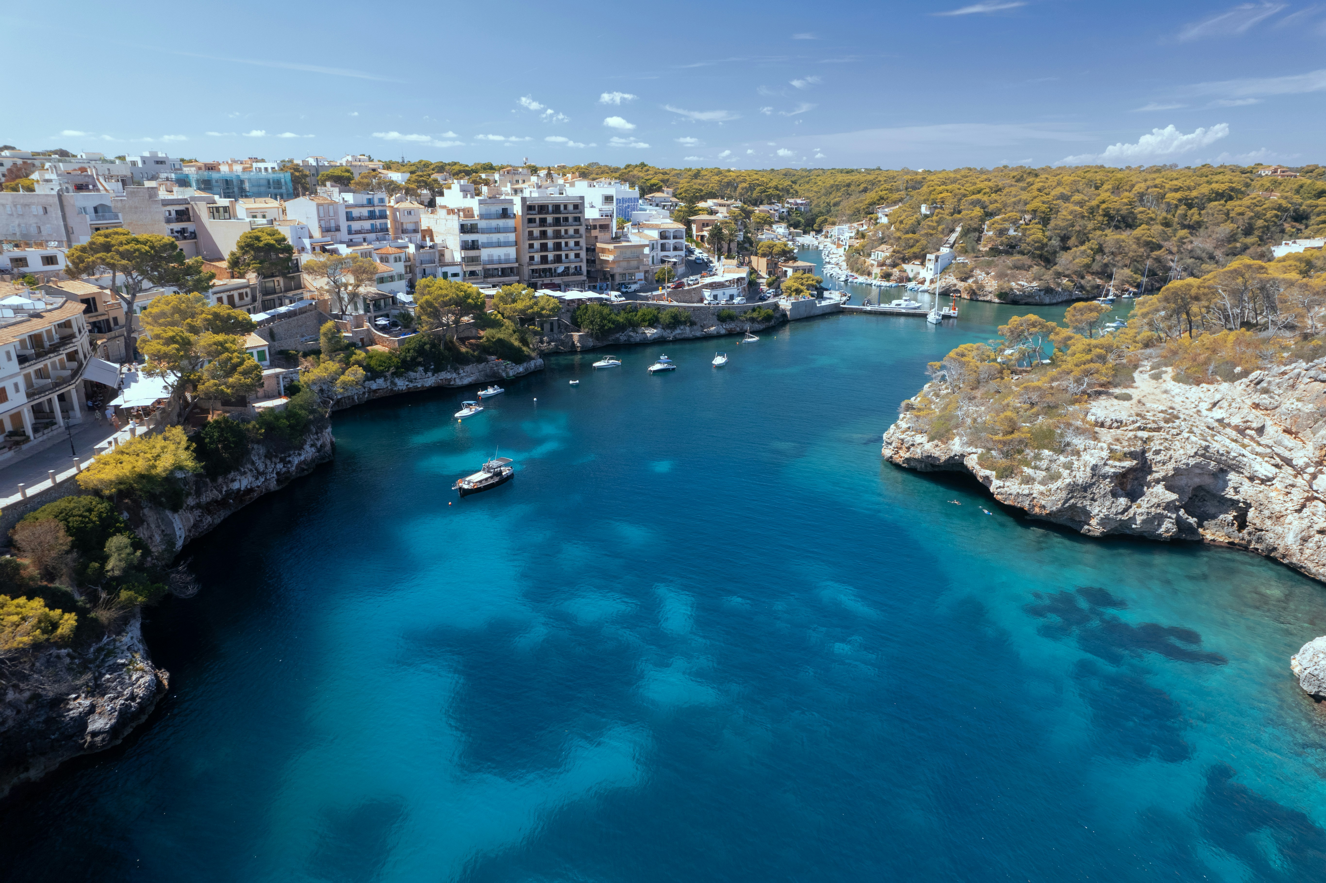 Coastal view of Cala Figuera, Mallorca, featuring turquoise waters, rocky cliffs, and a village with buildings nestled among trees