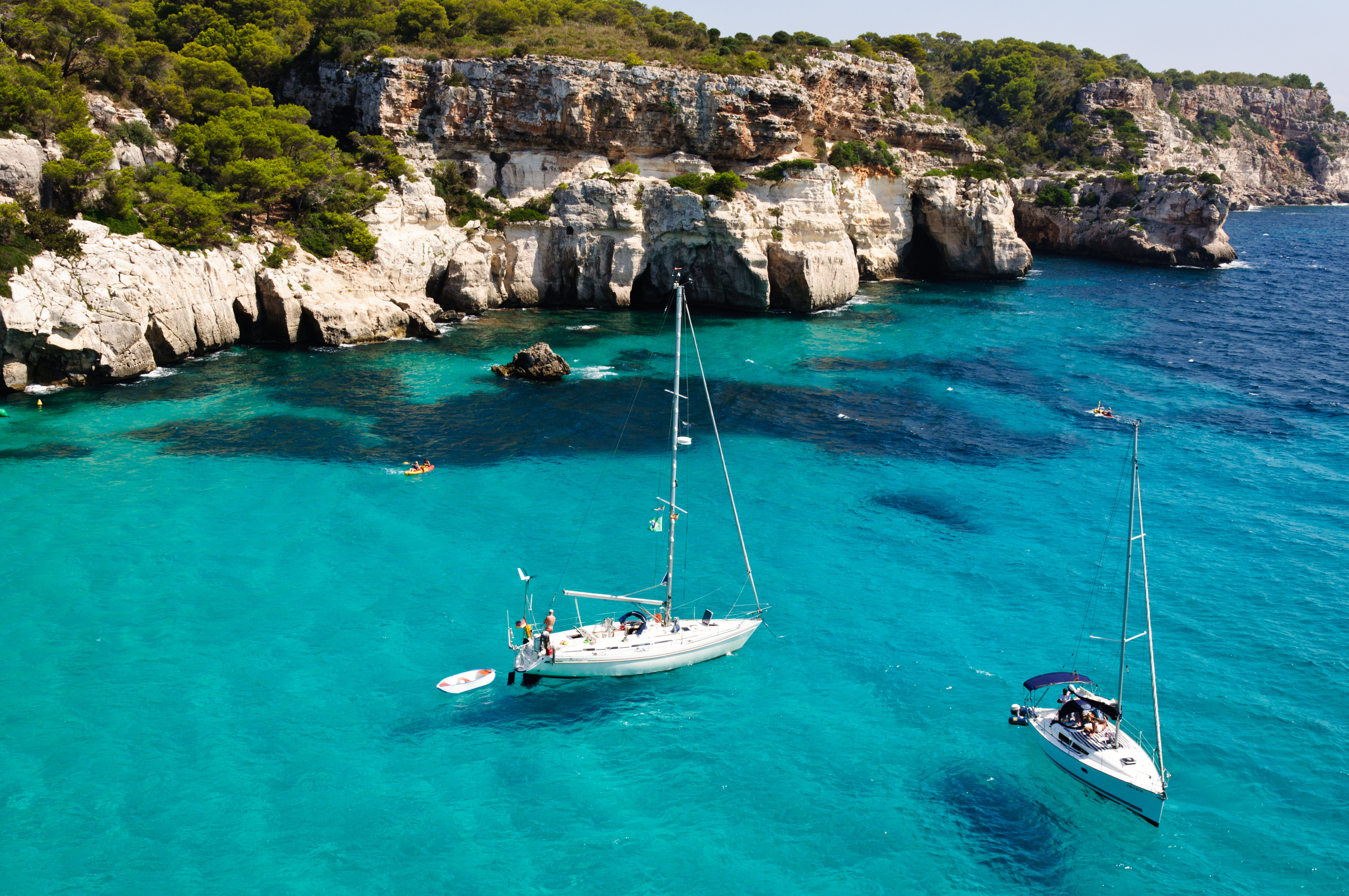 Sailboats cruising in clear turquoise waters near rocky cliffs and lush greenery in a coastal landscape