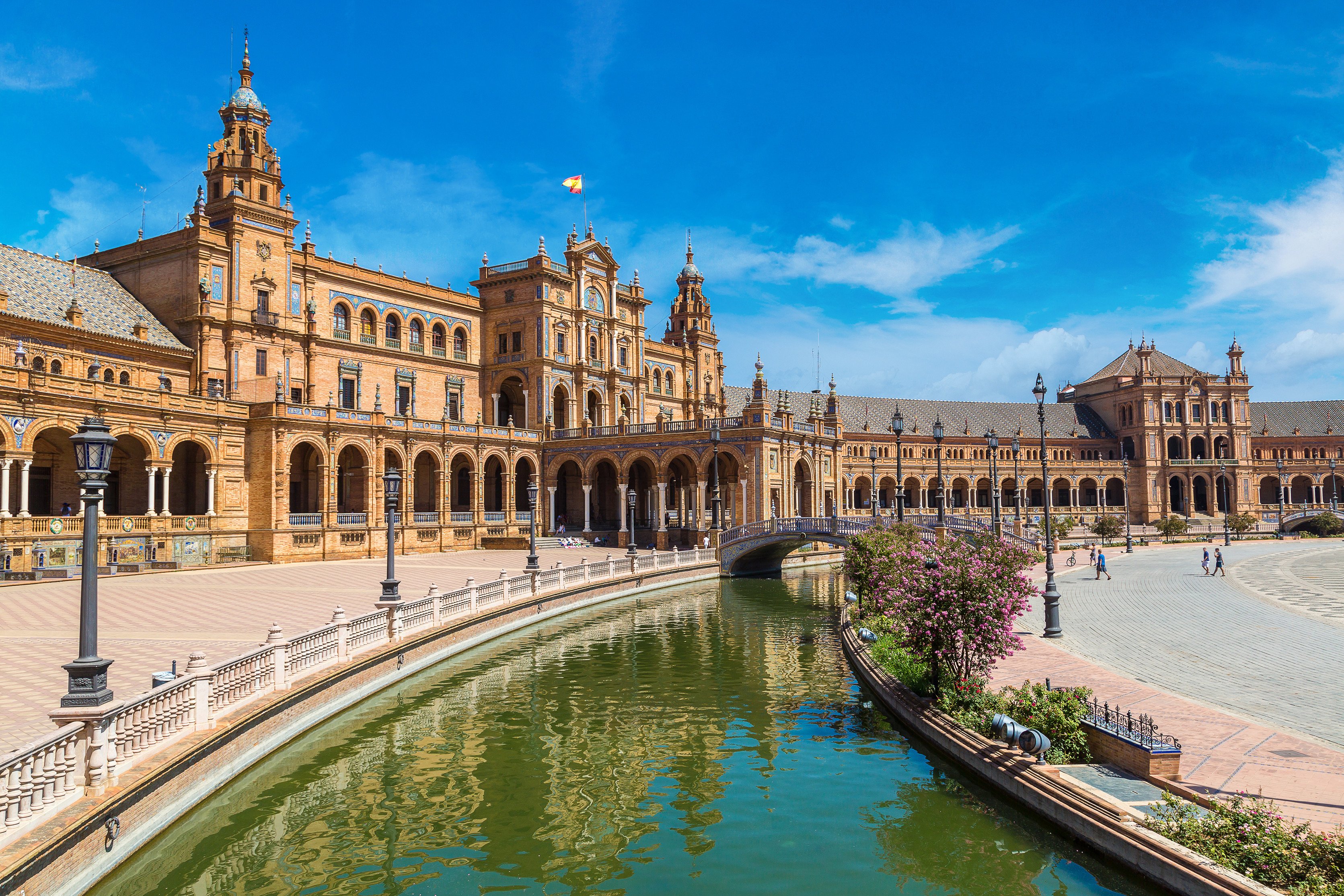 Plaza de España in Seville, Spain, showcasing its iconic architectural style with a surrounding canal and decorative bridges under a clear blue sky