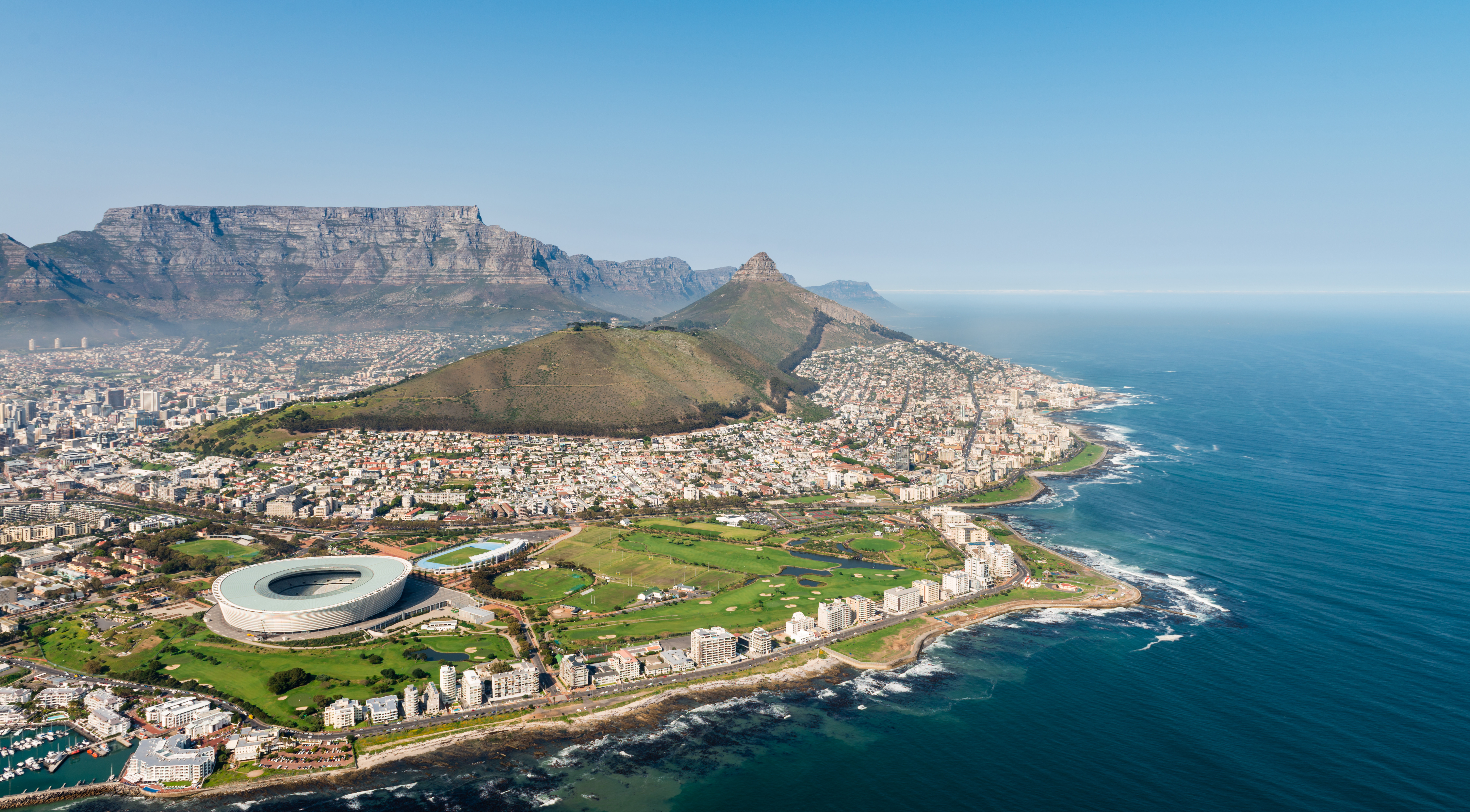 Aerial view of Cape Town, South Africa, featuring Table Mountain, Green Point Stadium, and the coastline along the Atlantic Ocean