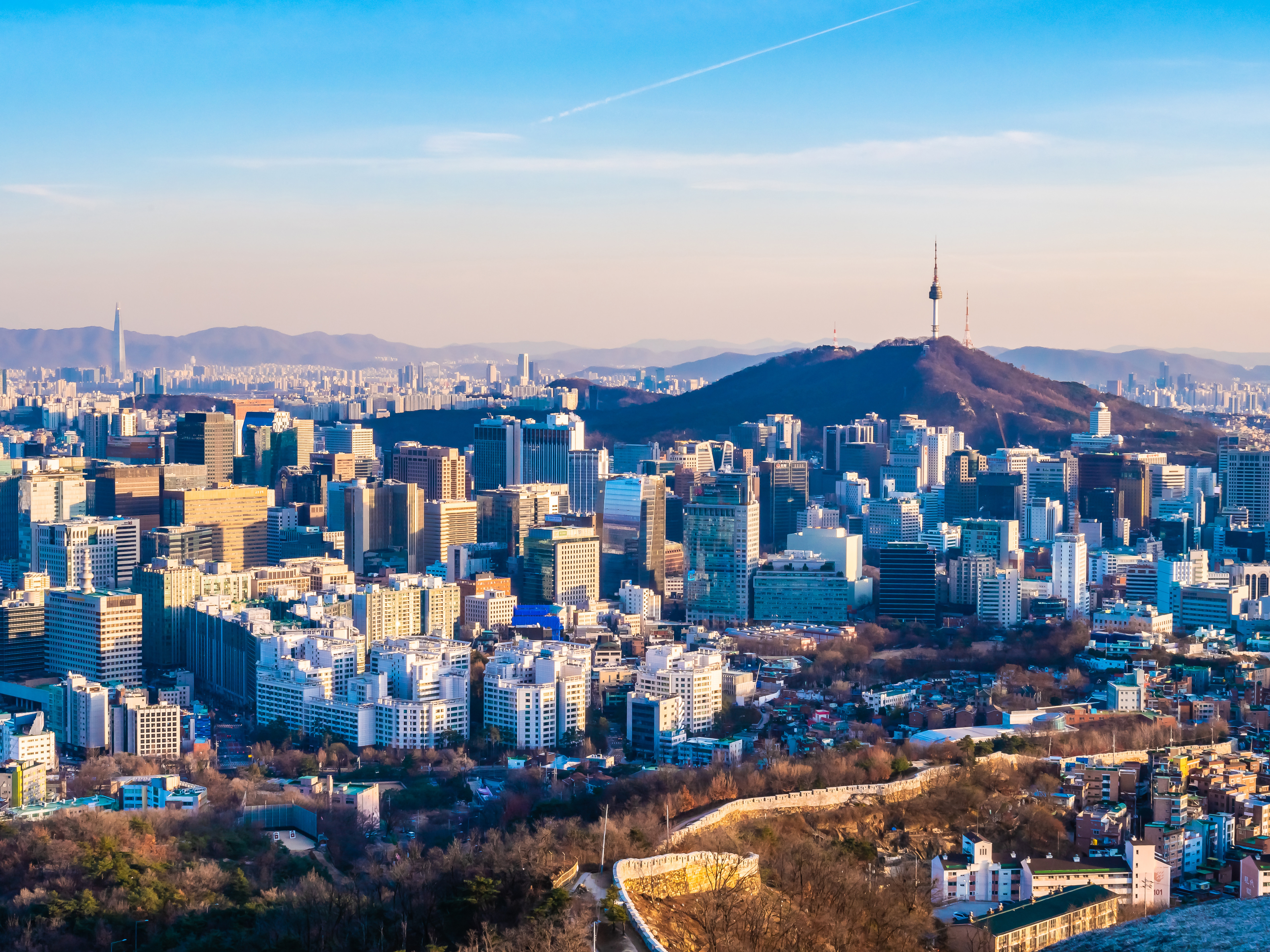 Seoul bysilhuett med Namsan-tårnet og fjell i bakgrunnen, som viser frem moderne skyskrapere og urbant landskap under en klar blå himmel