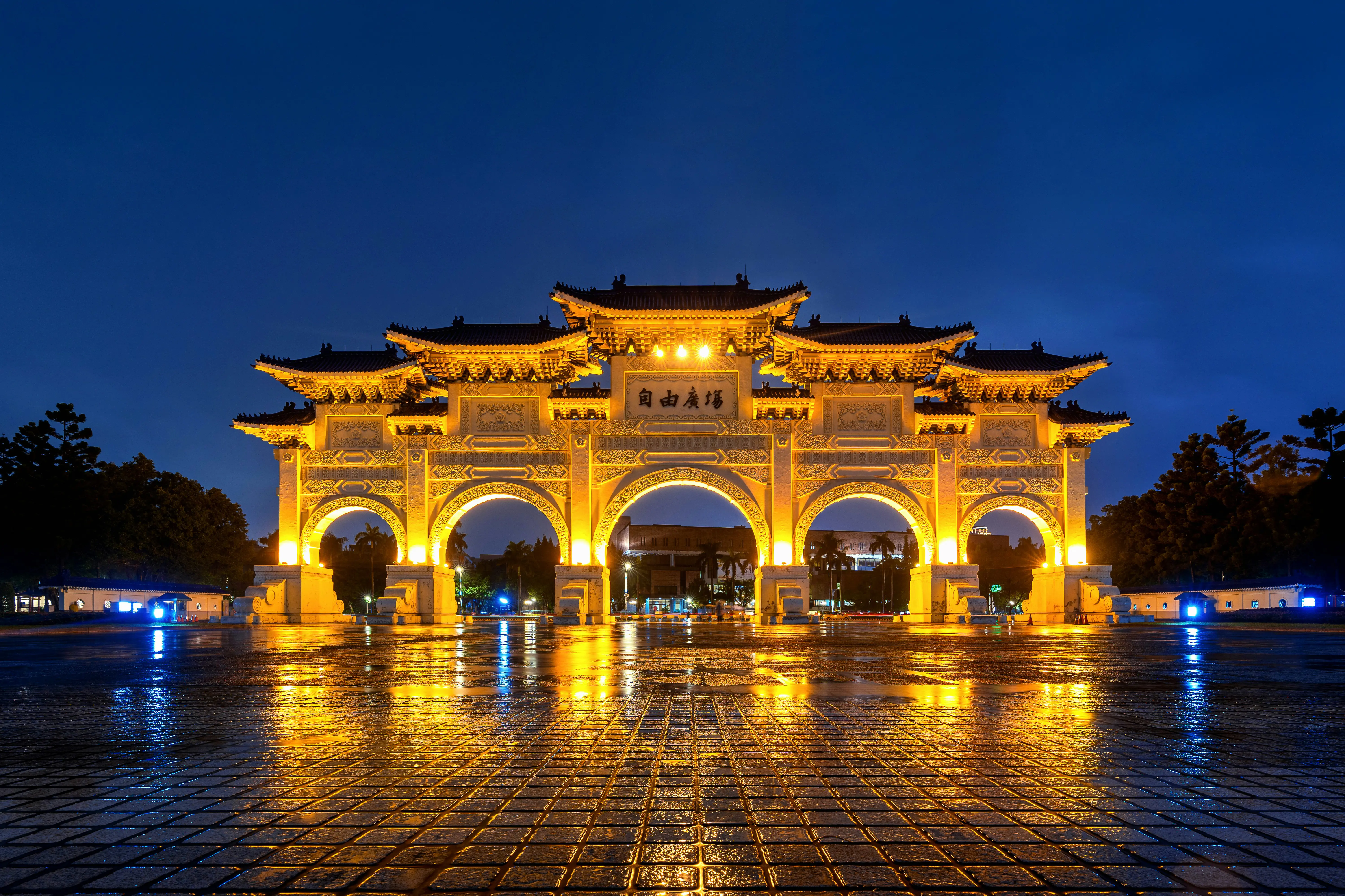 Opplyst Frihetsplassen i Taipei, Taiwan om natten, som viser tradisjonell kinesisk arkitektur med fargerik belysning som reflekterer på det våte fortauet