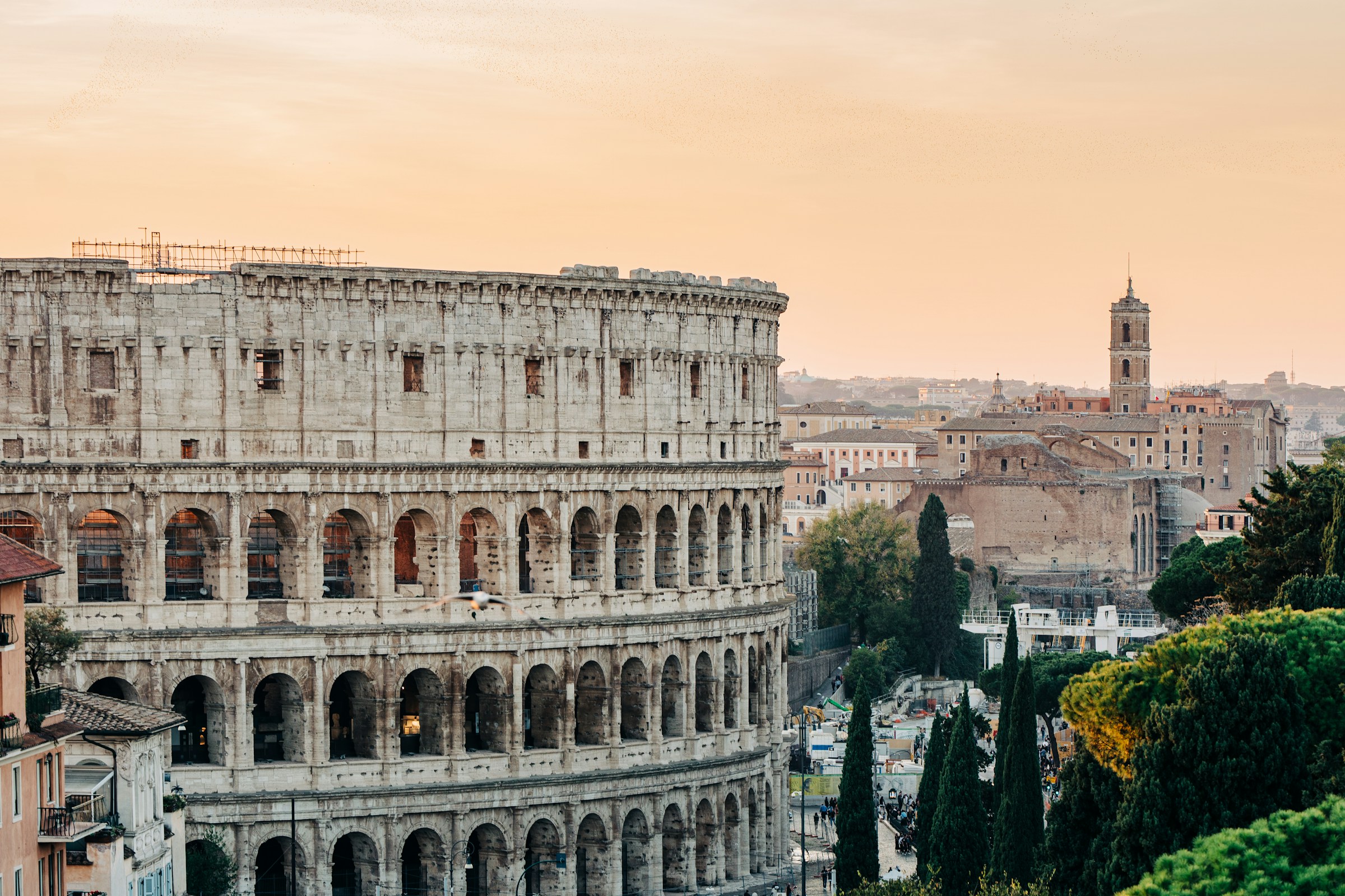 Colosseum in Rome at sunset, with ancient architecture and cityscape in the background.