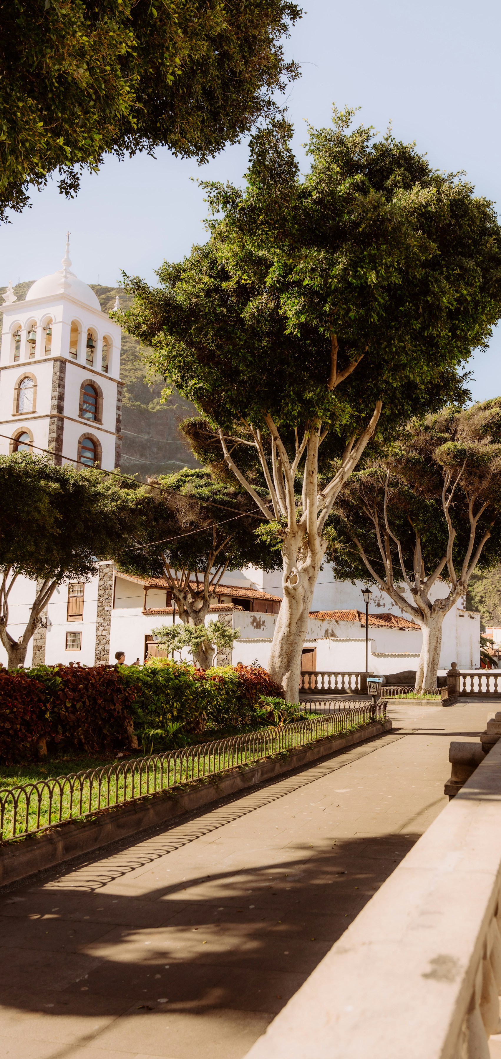 Historic church with white bell tower and stone accents surrounded by lush trees and a scenic pathway in a quaint European village