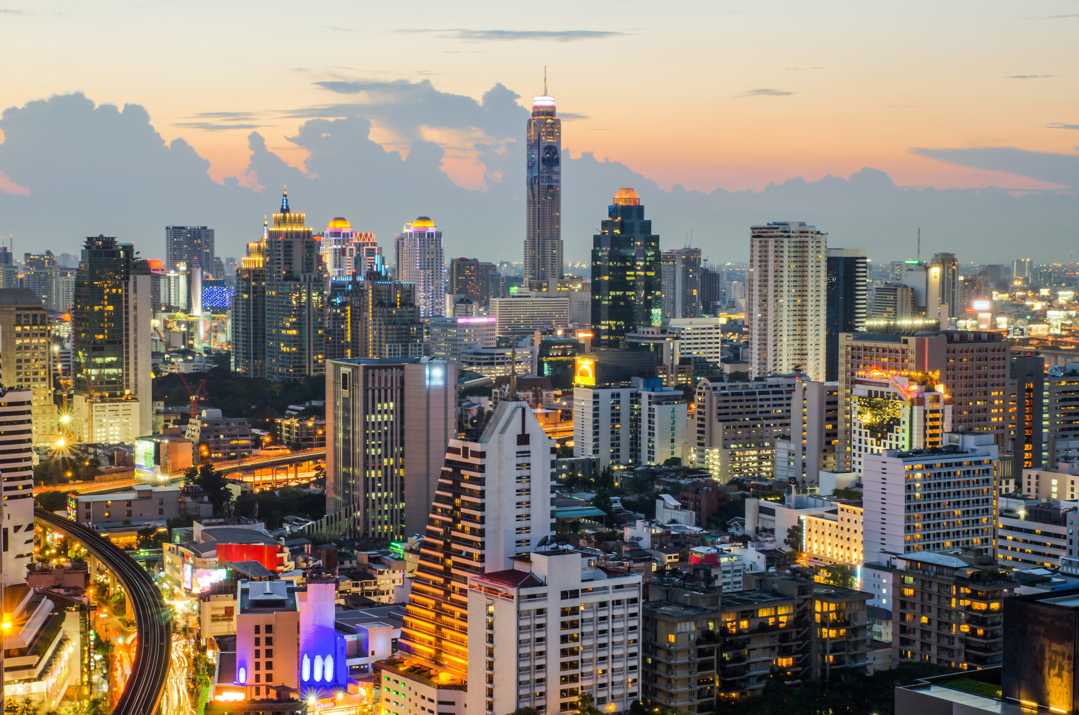 Travel to Bangkok - Cityscape at dusk with illuminated skyscrapers and a vibrant skyline against a colorful sunset.