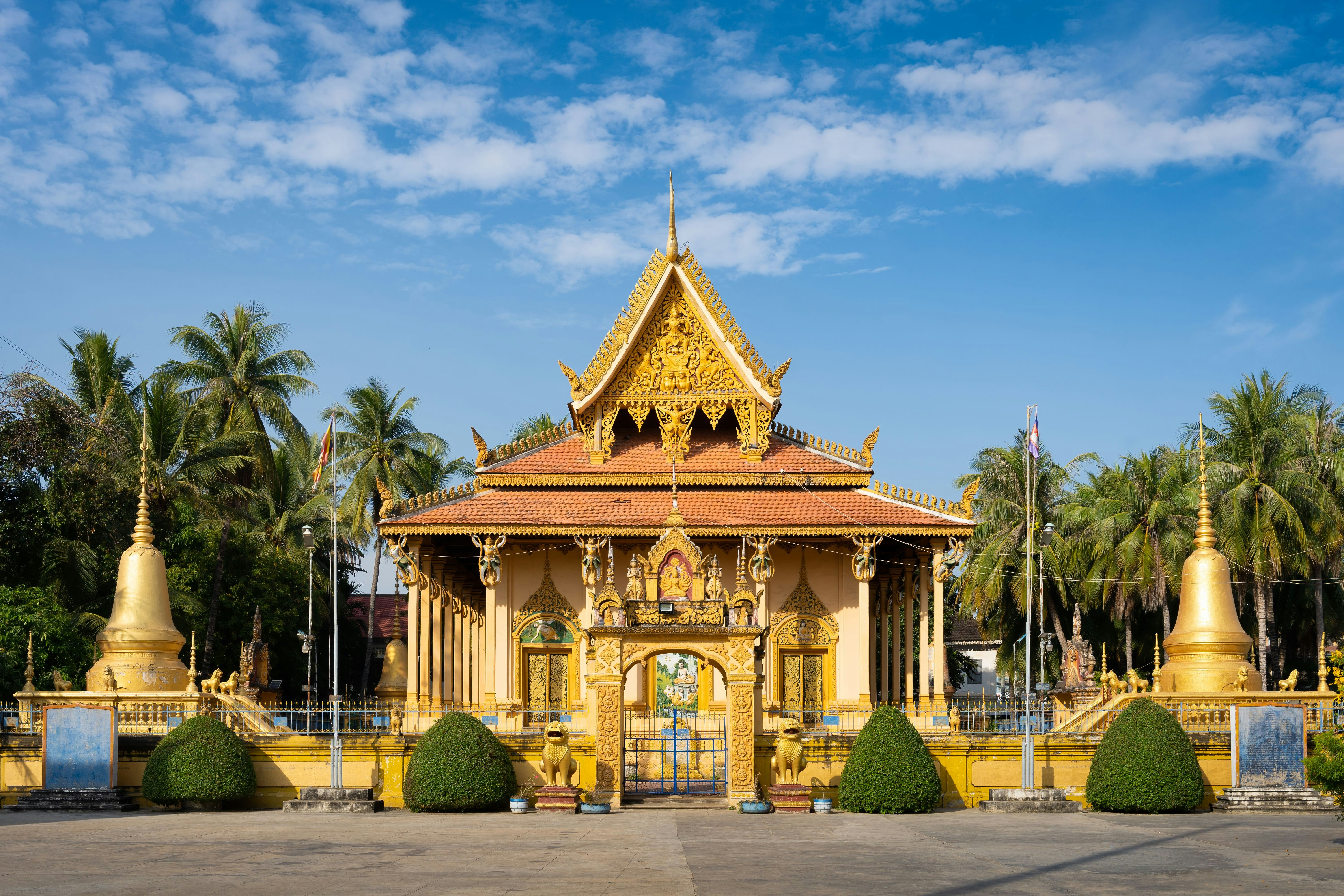 Golden Buddhist temple with intricate roof design surrounded by palm trees under a blue sky