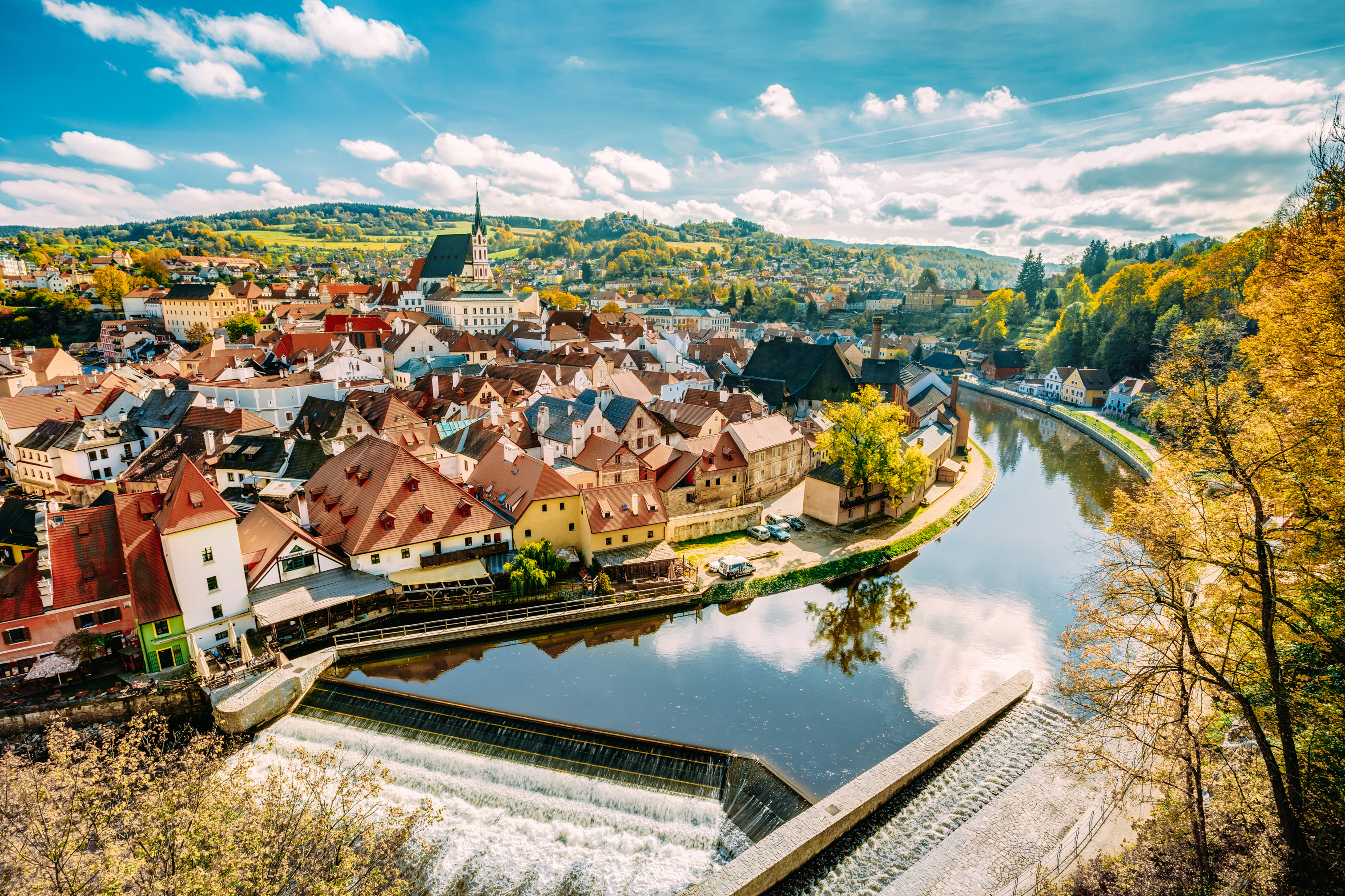 Panoramautsikt over Český Krumlov, en historisk by i Tsjekkia, med sjarmerende middelalderarkitektur, elven Vltava og frodig høstløv under en blå himmel