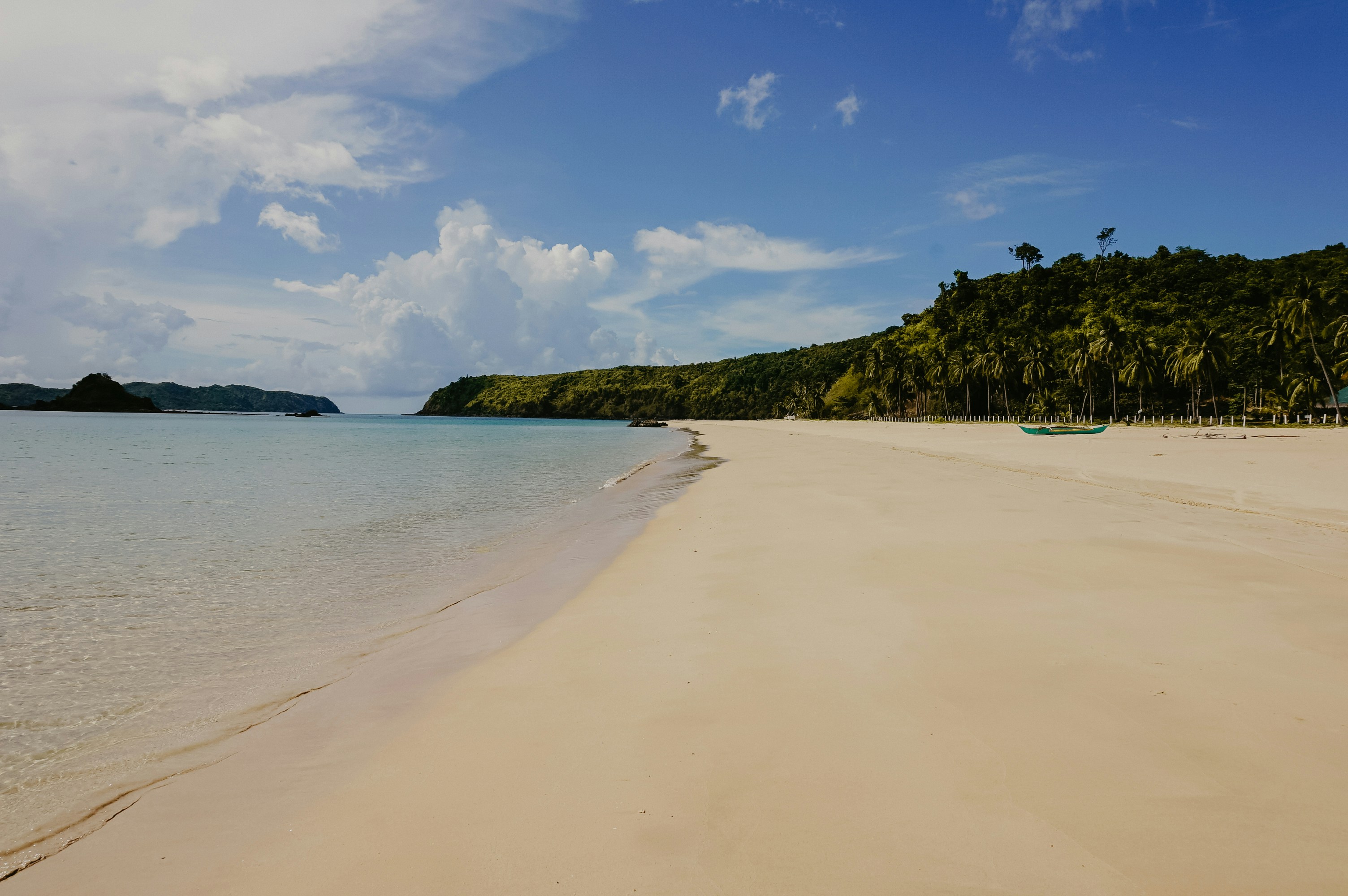 Sandstrand med klart blått vann og tredekkede åser under en solfylt himmel