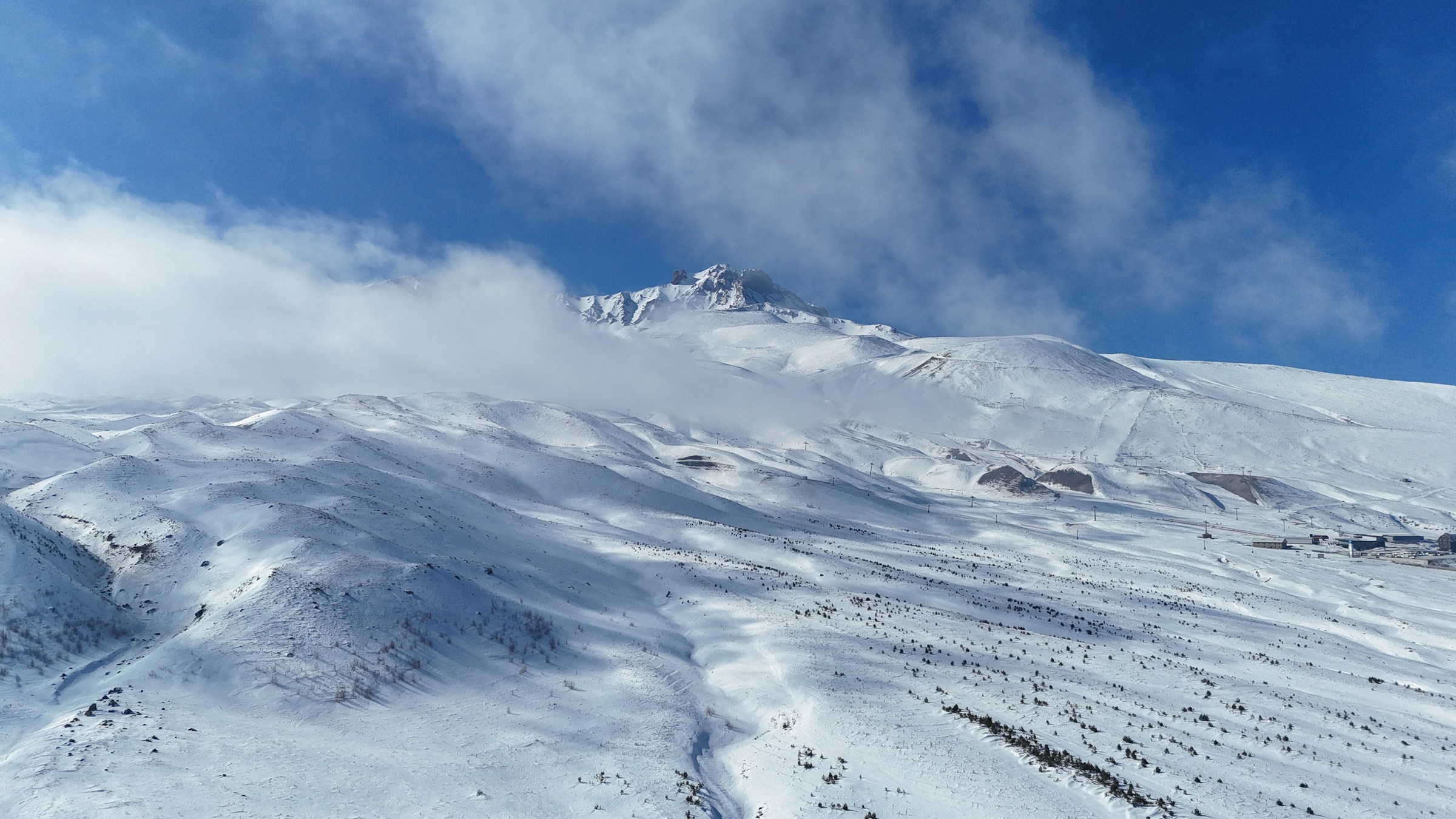 Snødekte fjell under en klar blå himmel med skyer på toppen av Erciyes, Tyrkia.